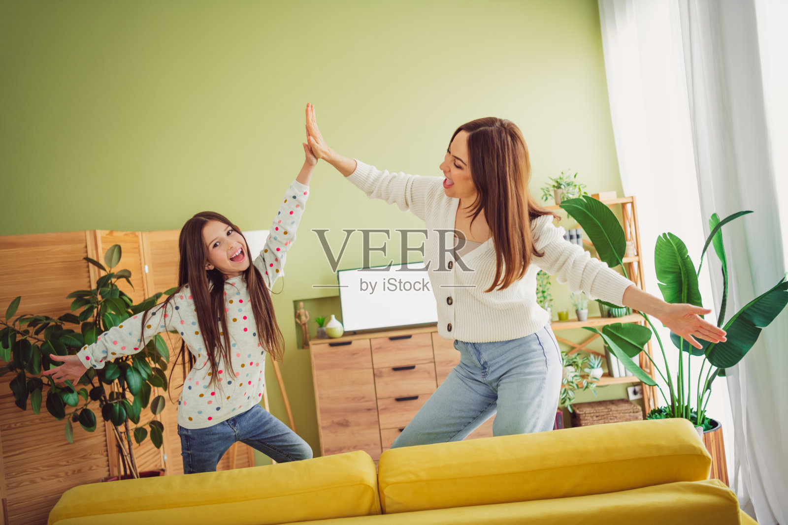 年轻母亲和女儿在阳光明媚的客厅里共享高五,享受轻松的春日时光。照片摄影图片