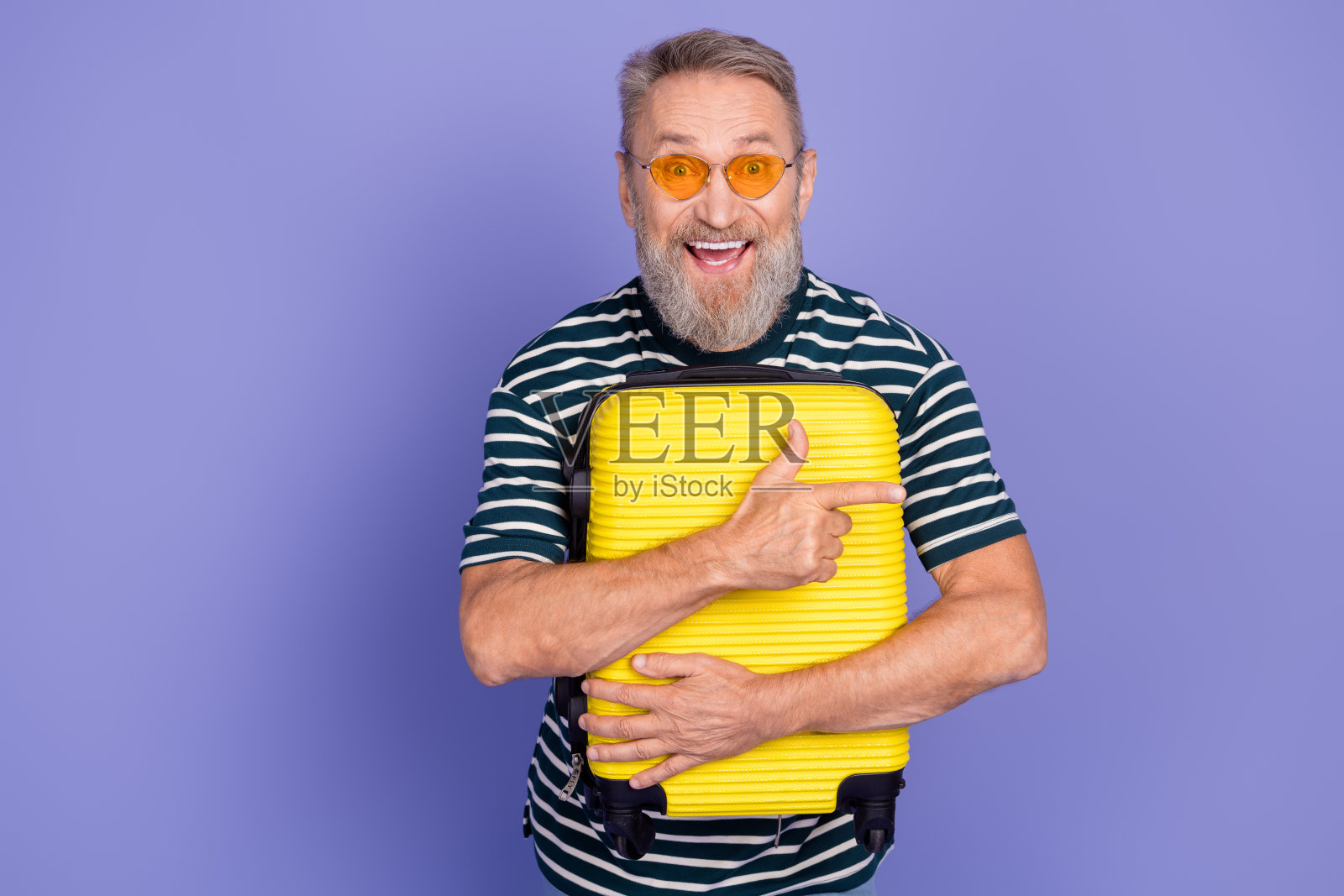 微笑的老年男子在紫色背景下手持黄色行李箱,表达出快乐和充满活力的休闲生活方式照片摄影图片