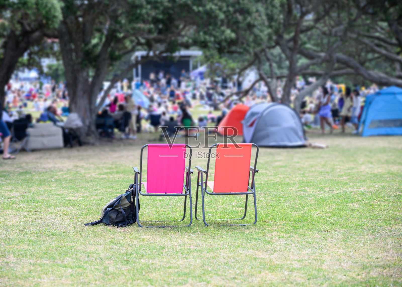 两个空的露营椅,无法辨认的人群在公园里聆听音乐会。奥克兰。照片摄影图片