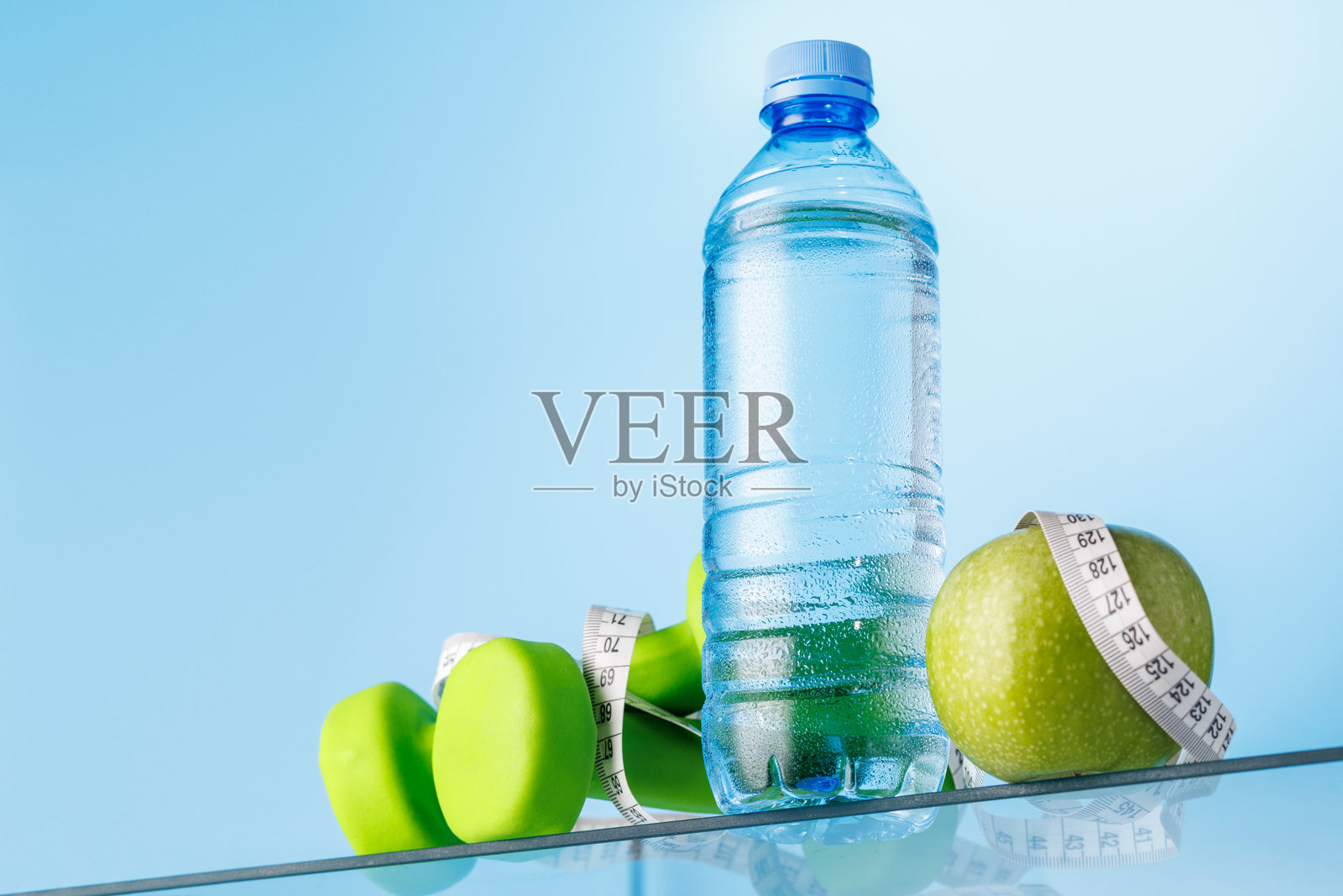 玻璃桌上的水瓶、绿苹果和哑铃照片摄影图片