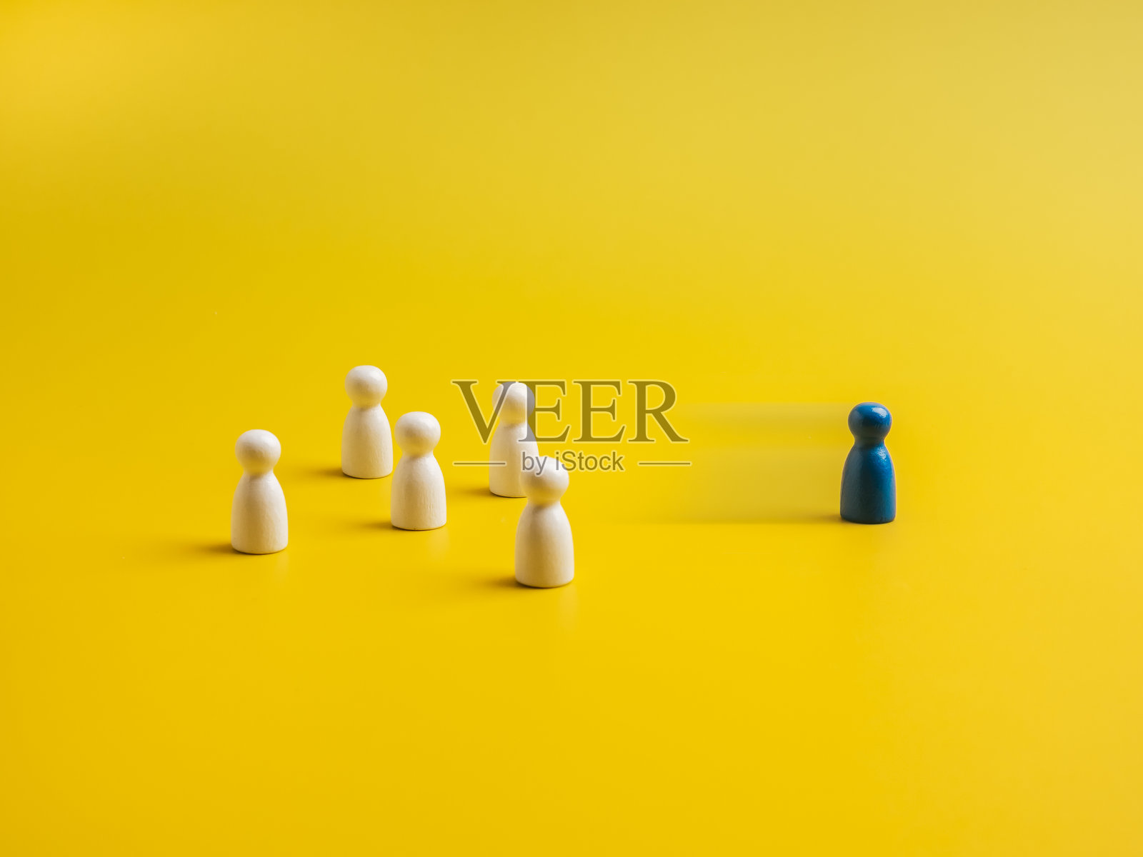 蓝色的不同者,从一群白色木偶人中走出,背景为黄色。突出于人群,领导力,独特,影响力,人才,差异概念。照片摄影图片