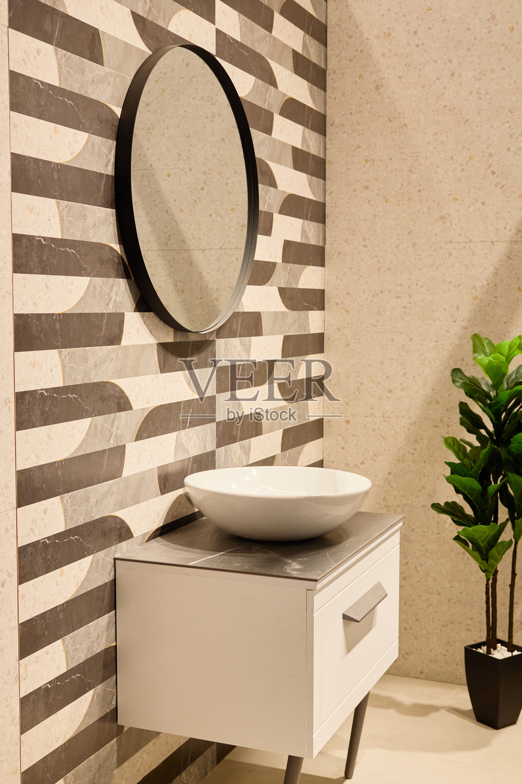 现代浴室展示了一个时尚的图案墙,灰白相间的条纹。白色梳妆台配有圆形洗手盆和圆形镜子,旁边还有一盆绿色植物。照片摄影图片