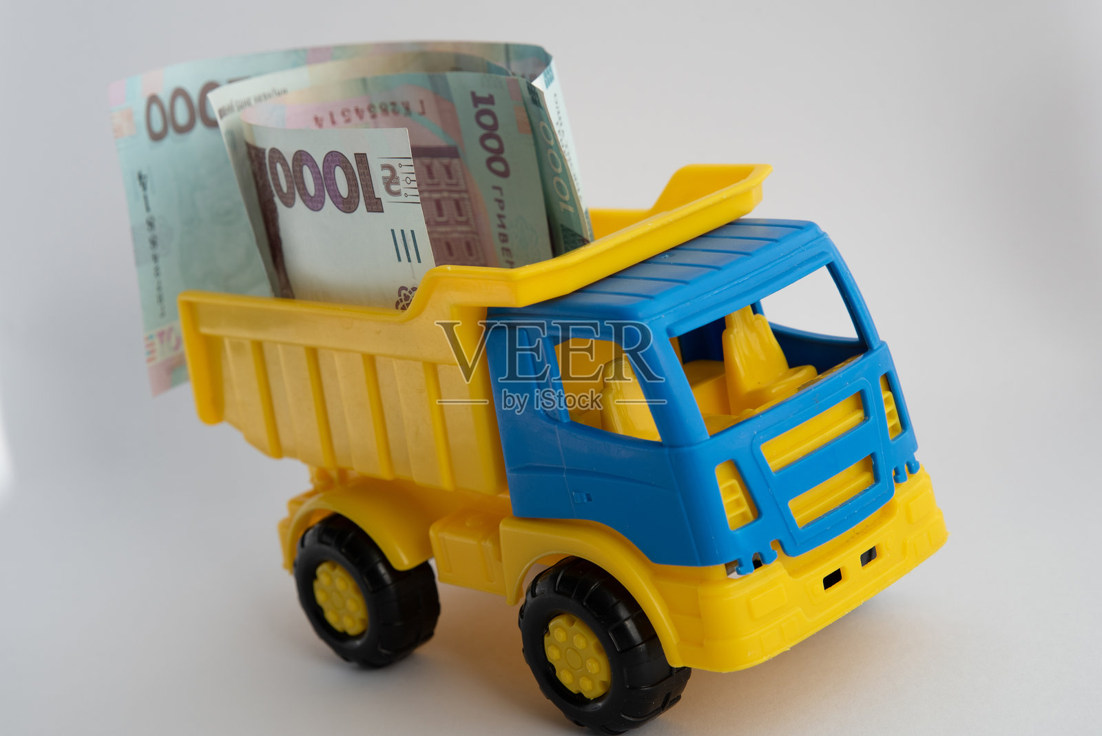 现金、钱,一辆黄色和蓝色的玩具车在白色背景上载着乌克兰格里夫纳纸币。照片摄影图片