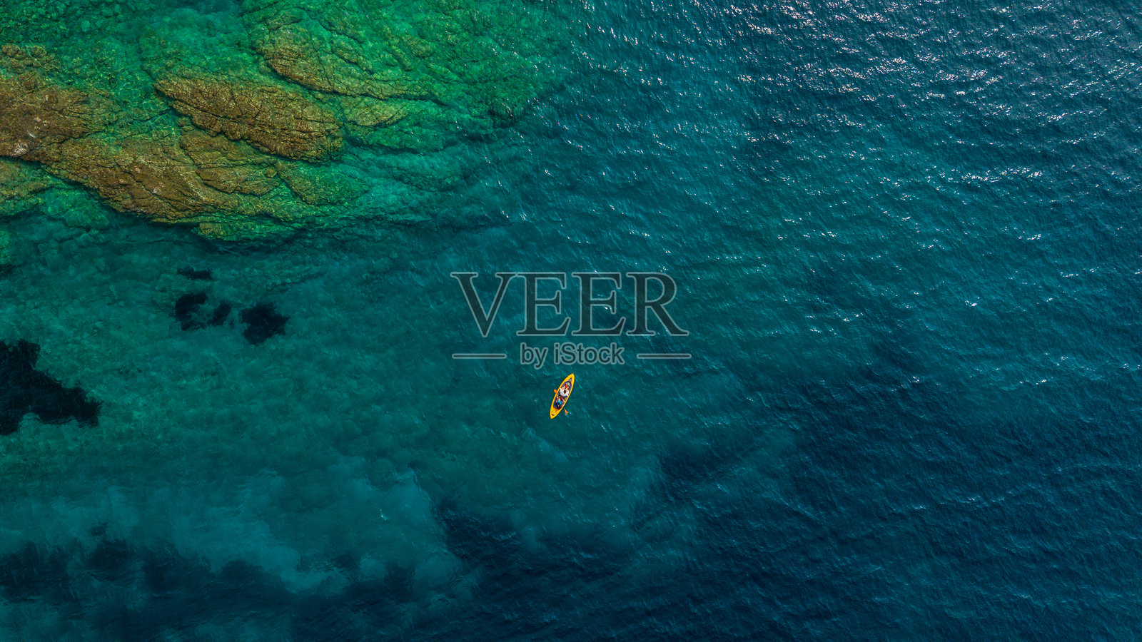 俯瞰两人在清澈的绿松石色岩石悬崖海岸上划独木舟的景象照片摄影图片