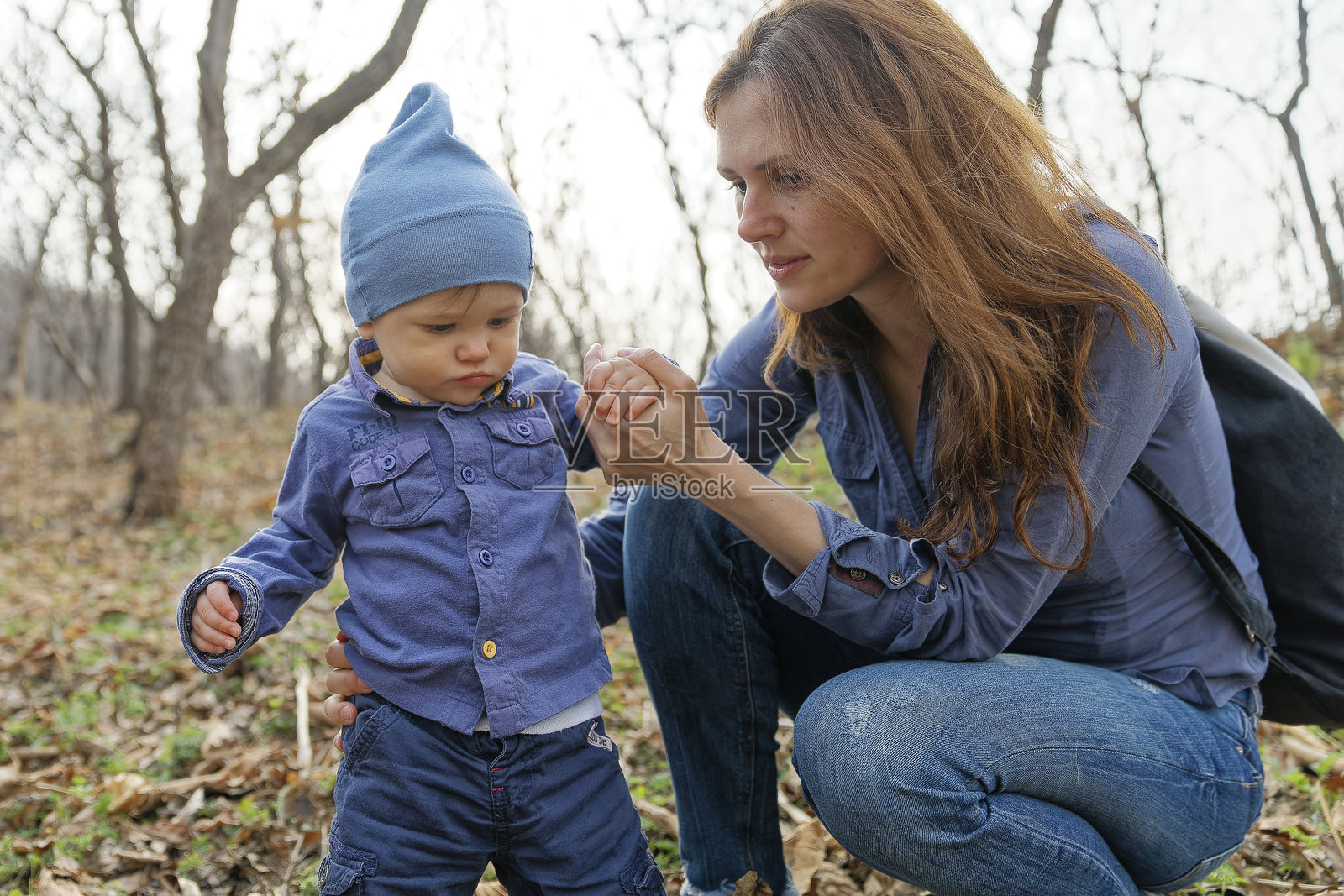 母亲和儿子在初春的森林中探险,孩子对大自然充满好奇,看到最后的秋叶和第一朵花。照片摄影图片