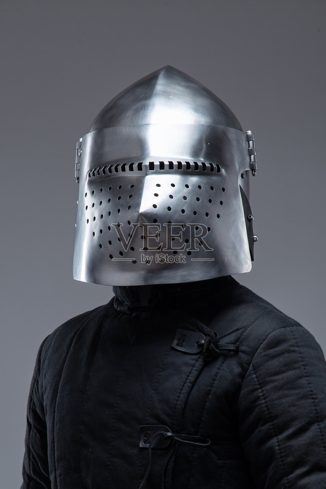 中世纪骑士头盔特写,带有穿孔面罩。此图像聚焦于一顶闪亮的金属头盔,面罩上有许多小孔,佩戴者身穿深色绗缝衣物。照片摄影图片