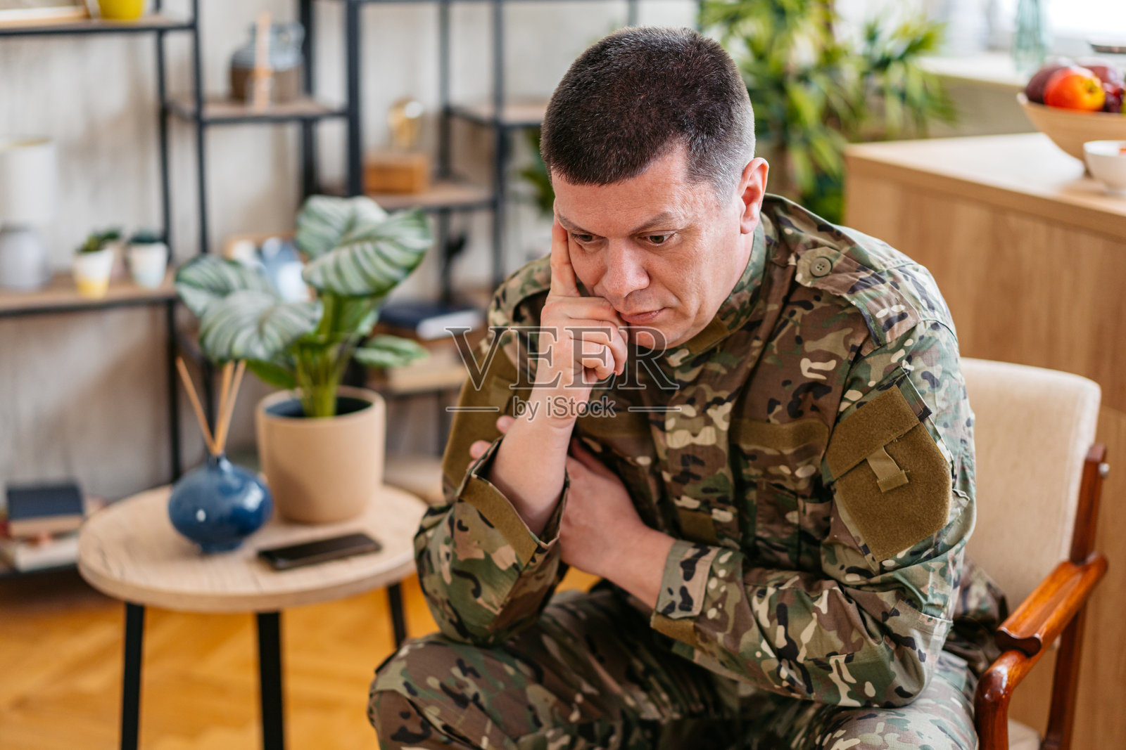 沮丧的中年士兵穿着军装坐在客厅的椅子上照片摄影图片