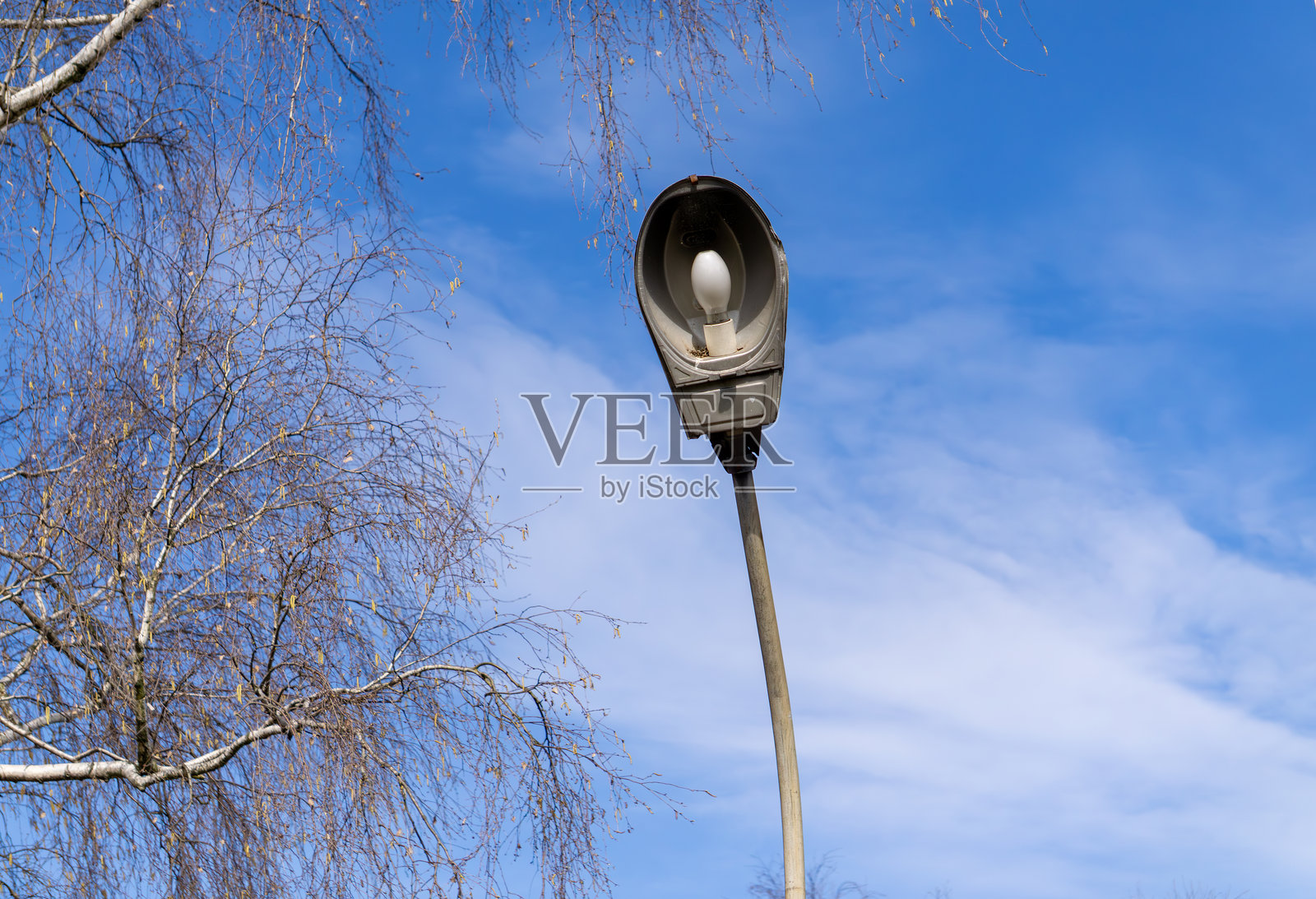 一盏旧破的街灯,弯曲的灯杆在略显多云的蓝天背景下。照片摄影图片