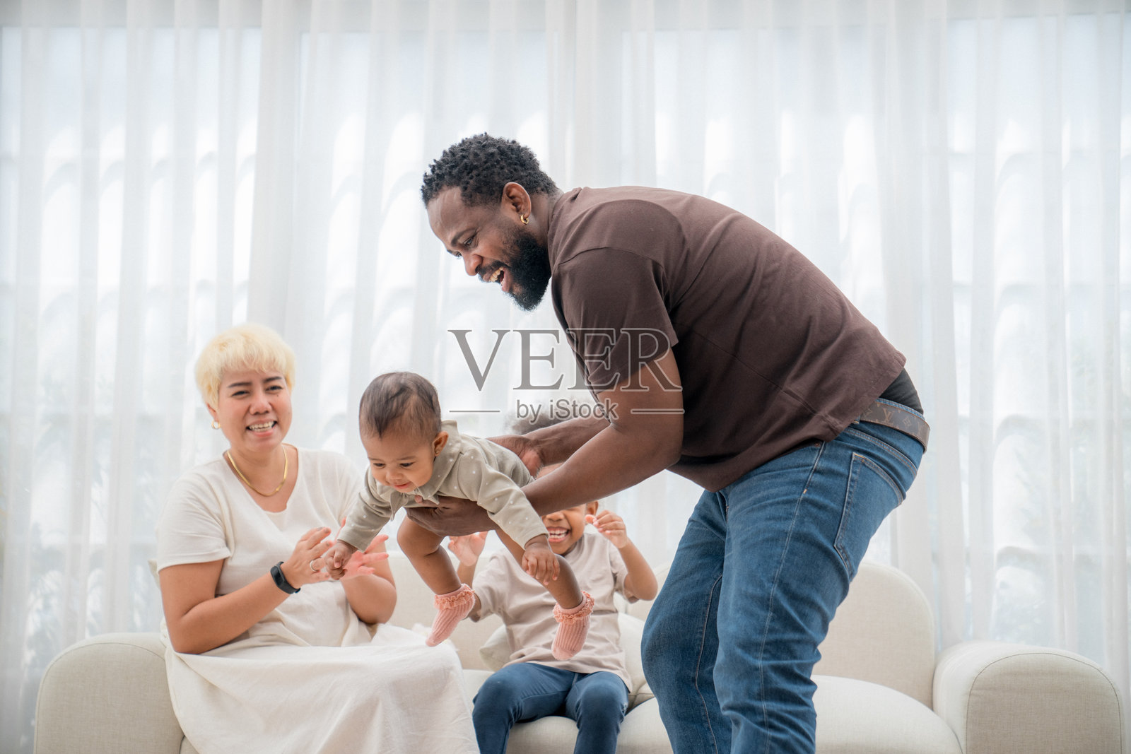 一家人在明亮的房间里与婴儿一起享受快乐的室内时光,脸上洋溢着愉悦的表情。照片摄影图片