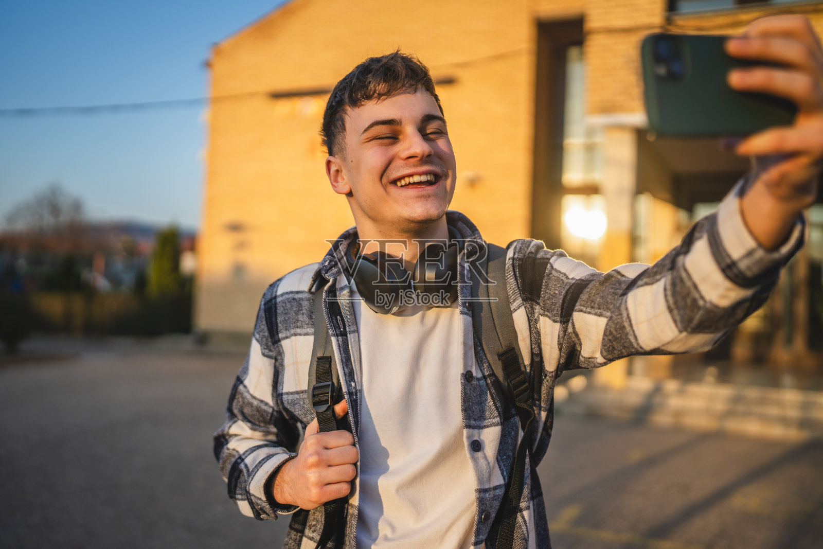 男学生站在大学前面,正在用手机进行视频通话。照片摄影图片