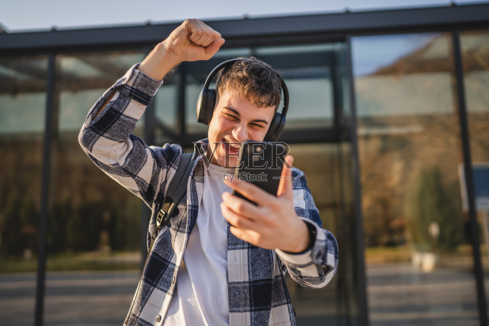 年轻男学生站在现代建筑前使用手机照片摄影图片