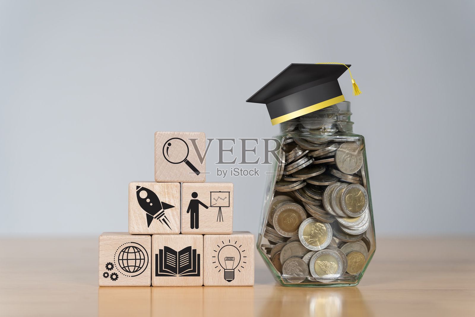 玻璃罐中的一堆硬币,木块上放着毕业帽。为教育储蓄的概念照片摄影图片