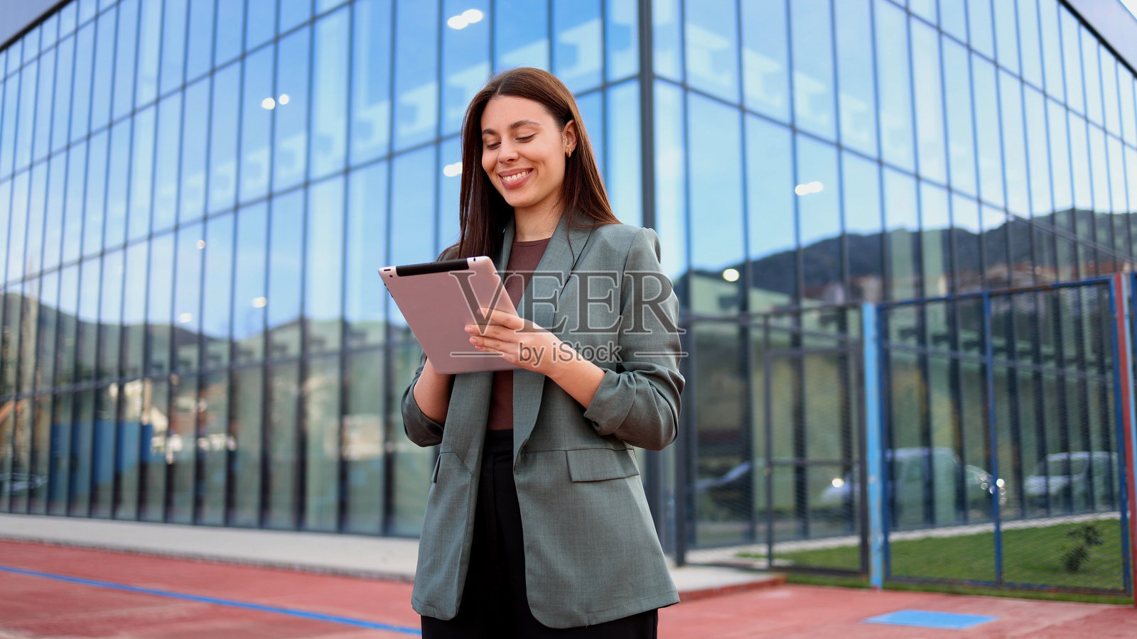 在现代办公大楼前微笑着手持平板的女商人照片摄影图片