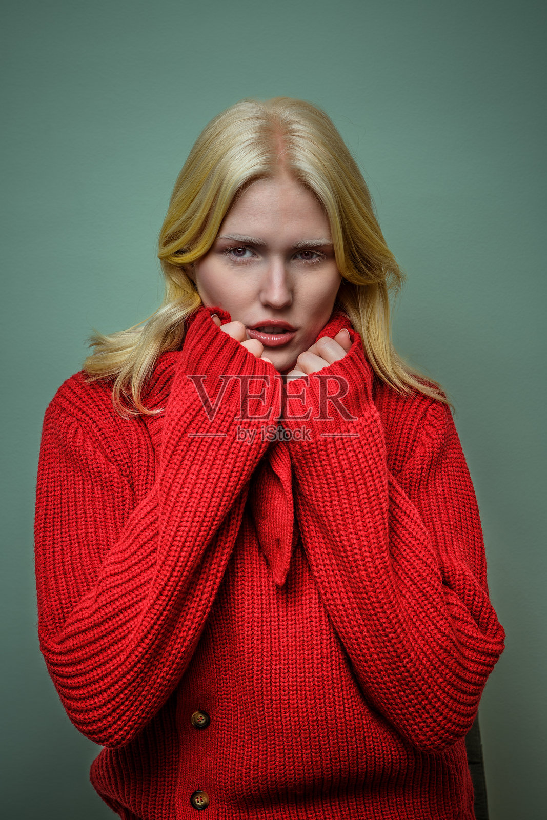 穿着舒适红色毛衣、表情严肃的年轻女性,背景为柔和的绿色。照片摄影图片