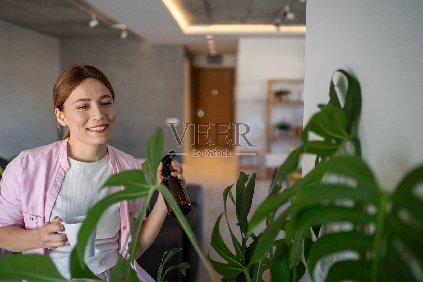 女性在现代公寓里一边喝咖啡一边给植物浇水照片摄影图片