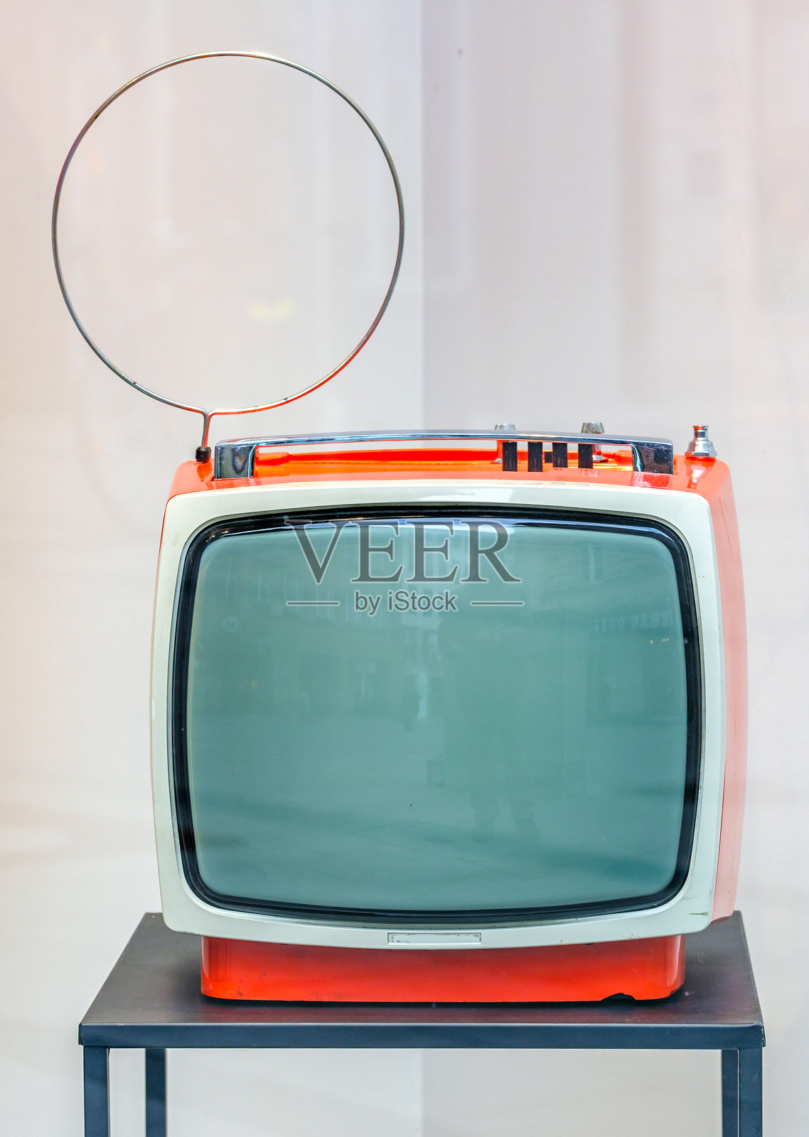 复古橙色电视机带天线,放置在黑色金属支架上,背景为浅色,展示复古设计元素。照片摄影图片