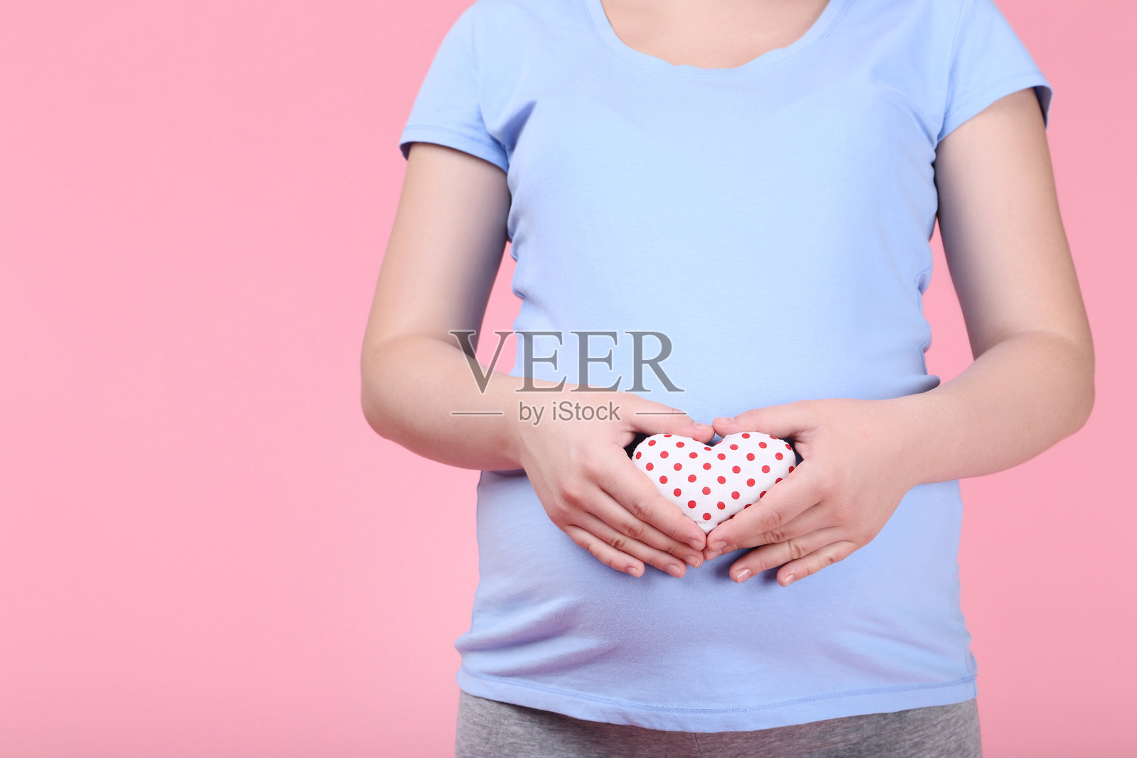 怀孕的女人在粉色背景上捧着布制心形物品照片摄影图片