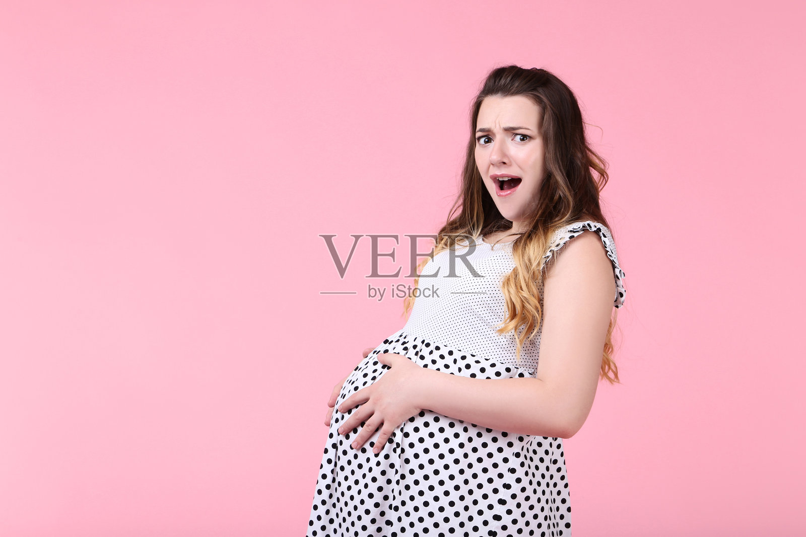 美丽的孕妇穿着时尚裙子,背景为粉色照片摄影图片