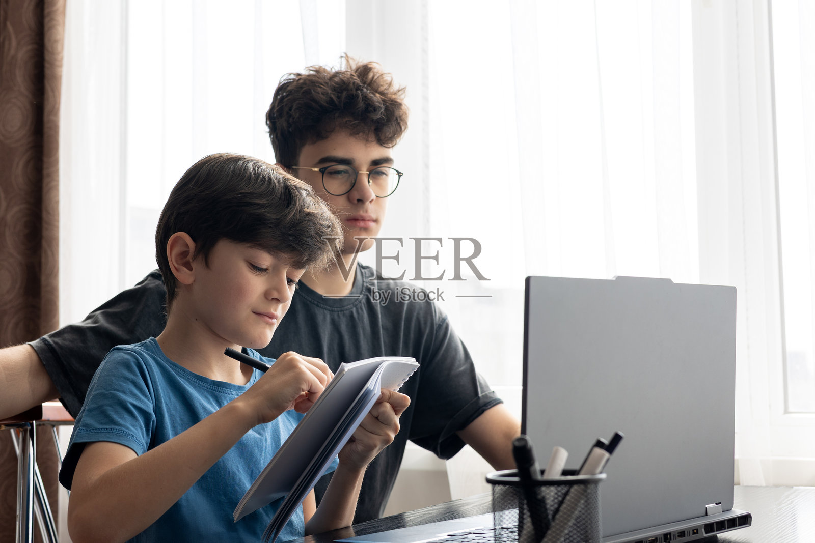 两个兄弟专注于笔记本电脑屏幕,沉浸在思考和学习中。在线学习。远程教育。代际互动。现代儿童与电子设备。学习时的专注。照片摄影图片
