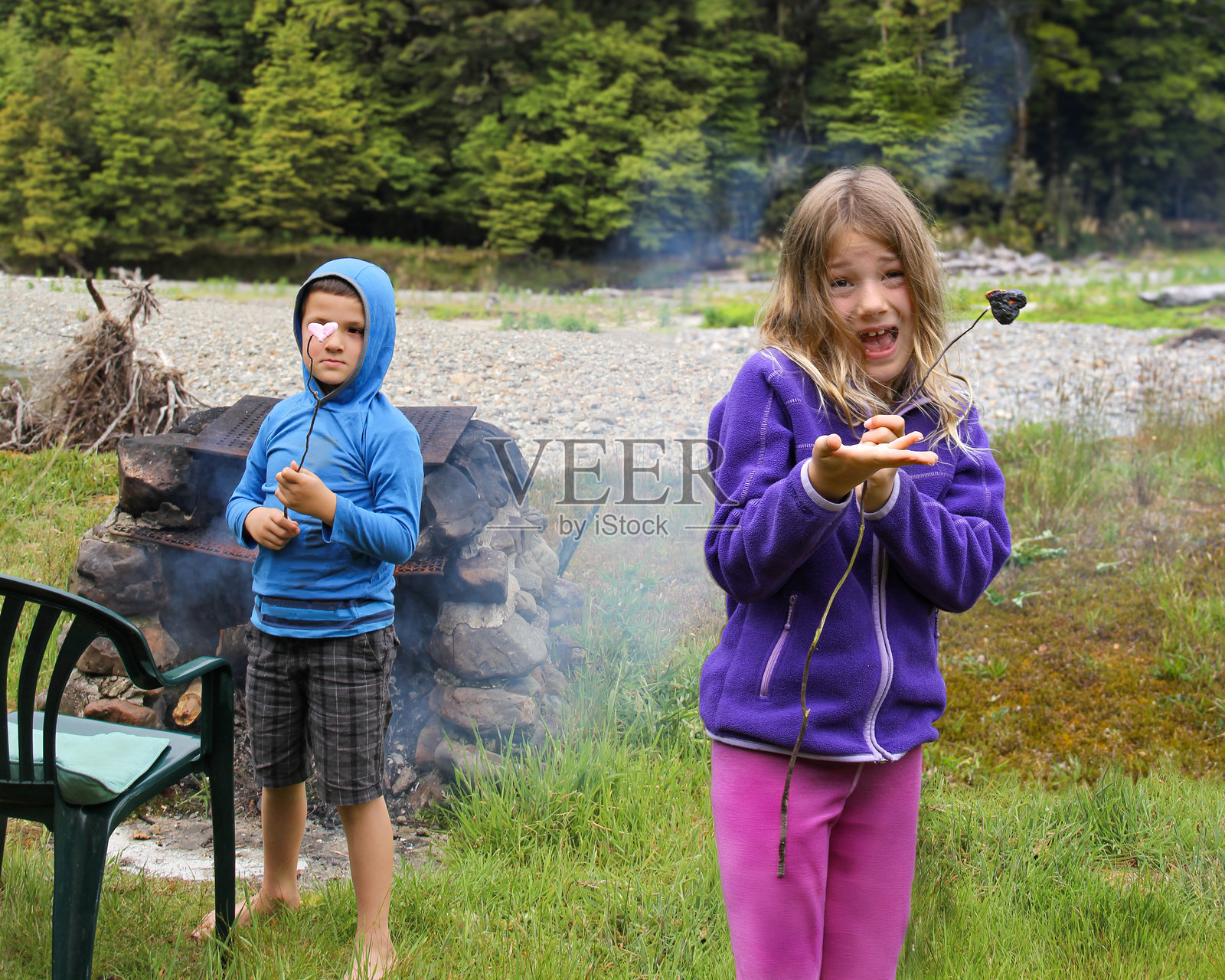 女孩手里拿着烤焦的棉花糖,小弟弟正准备烤他的棉花糖。照片摄影图片