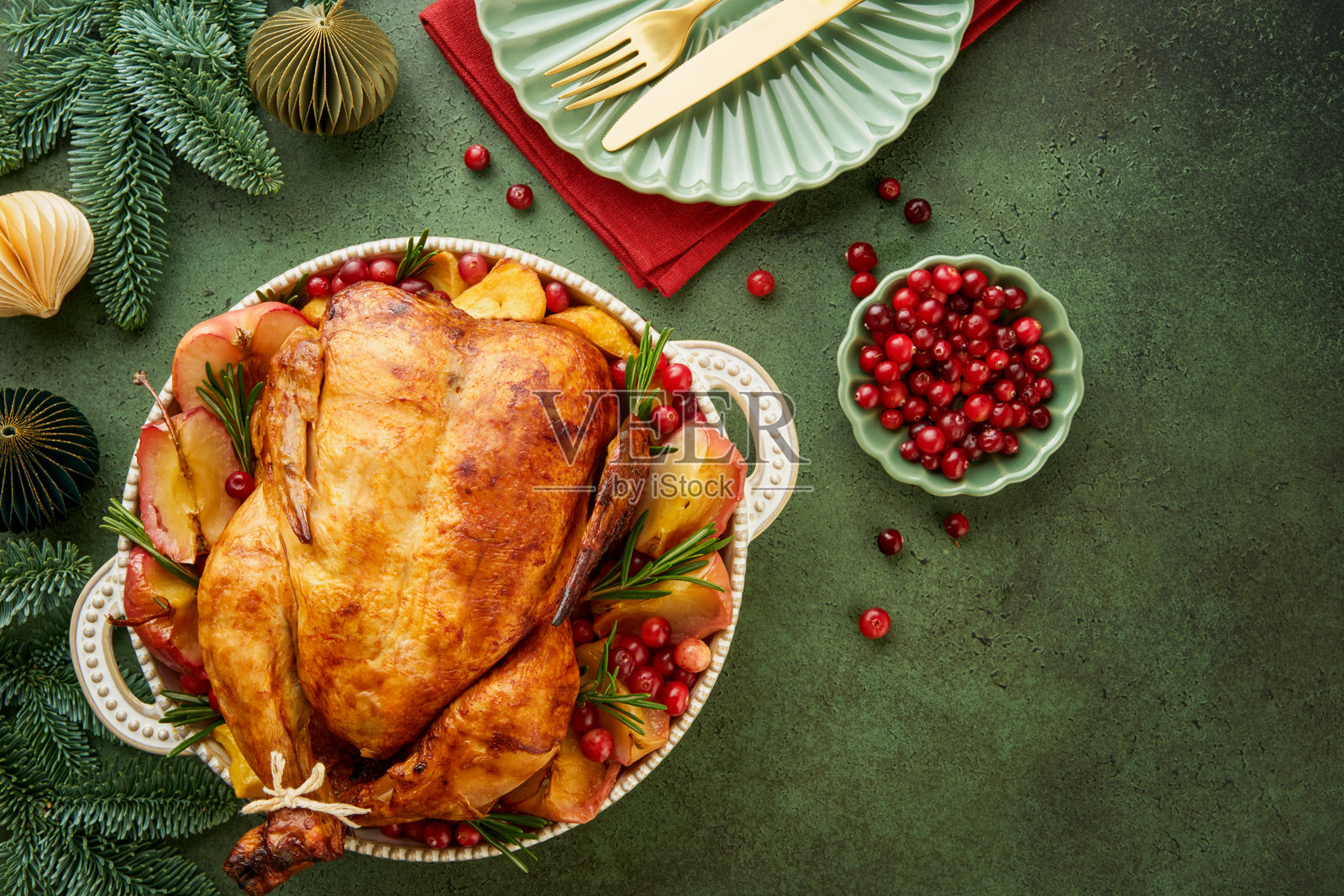 圣诞节烤鸡配苹果、土豆、蔓越莓、酱汁和香草,摆放在绿色大理石背景的大盘子上。节日家庭禽类菜肴。俯视图。留白空间。照片摄影图片