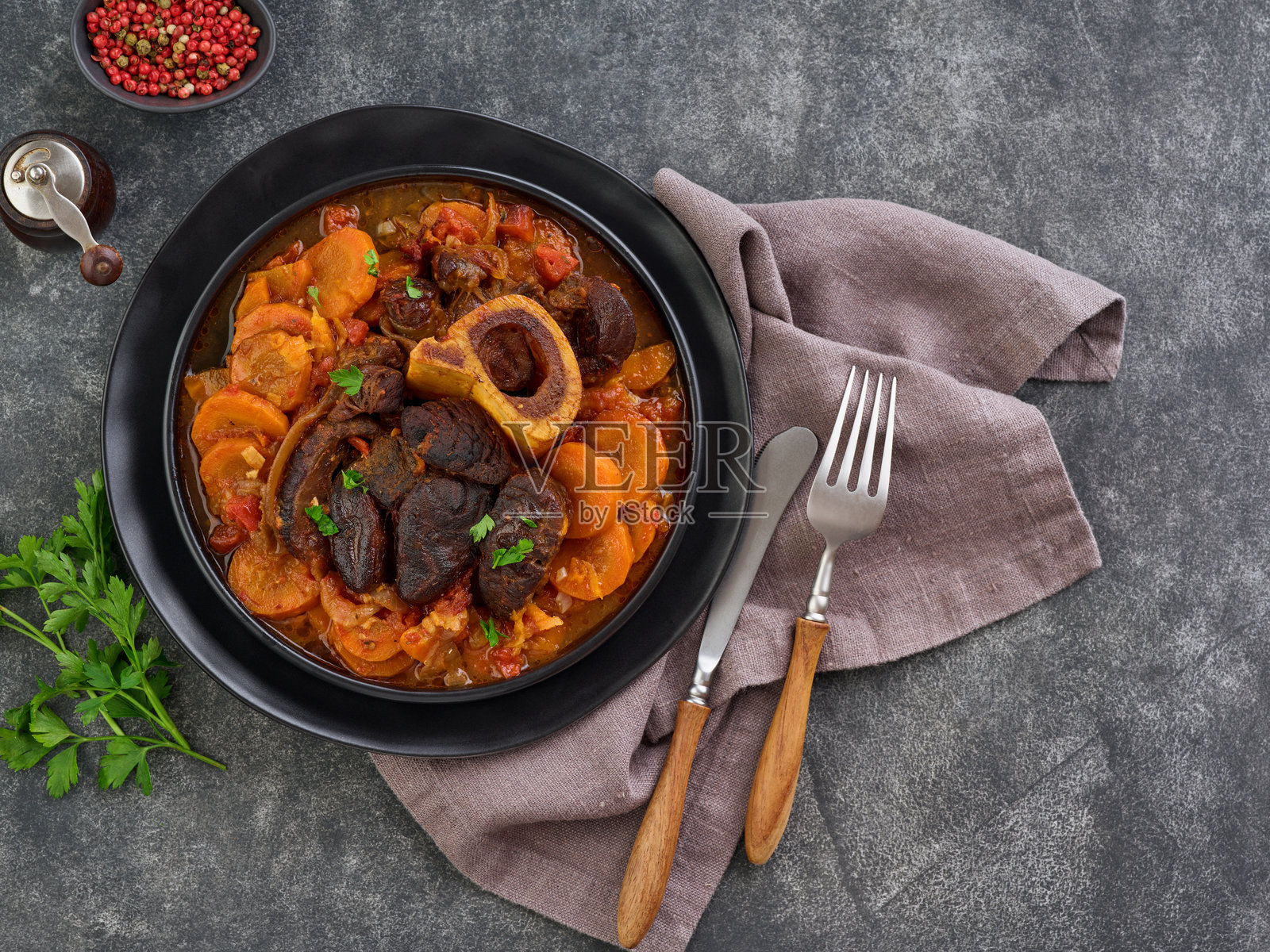 意大利炖小牛膝,配有蔬菜酱和香料,背景为旧混凝土桌面。照片摄影图片