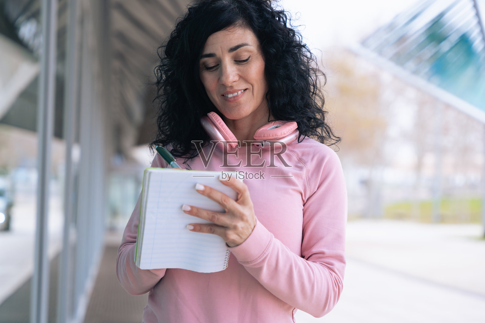穿着粉色连帽衫的白人女性运动员戴着耳机在笔记本上写字照片摄影图片