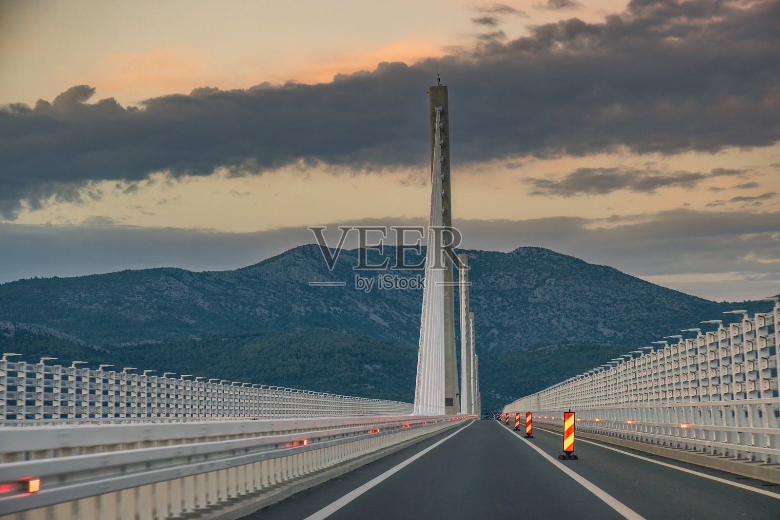 克罗地亚佩尔耶萨茨半岛的佩尔耶萨茨大桥。黄昏时分,驾车穿越现代化的桥梁,桥梁由高耸的支柱支撑,背景是多云的天空和遥远的山脉。照片摄影图片