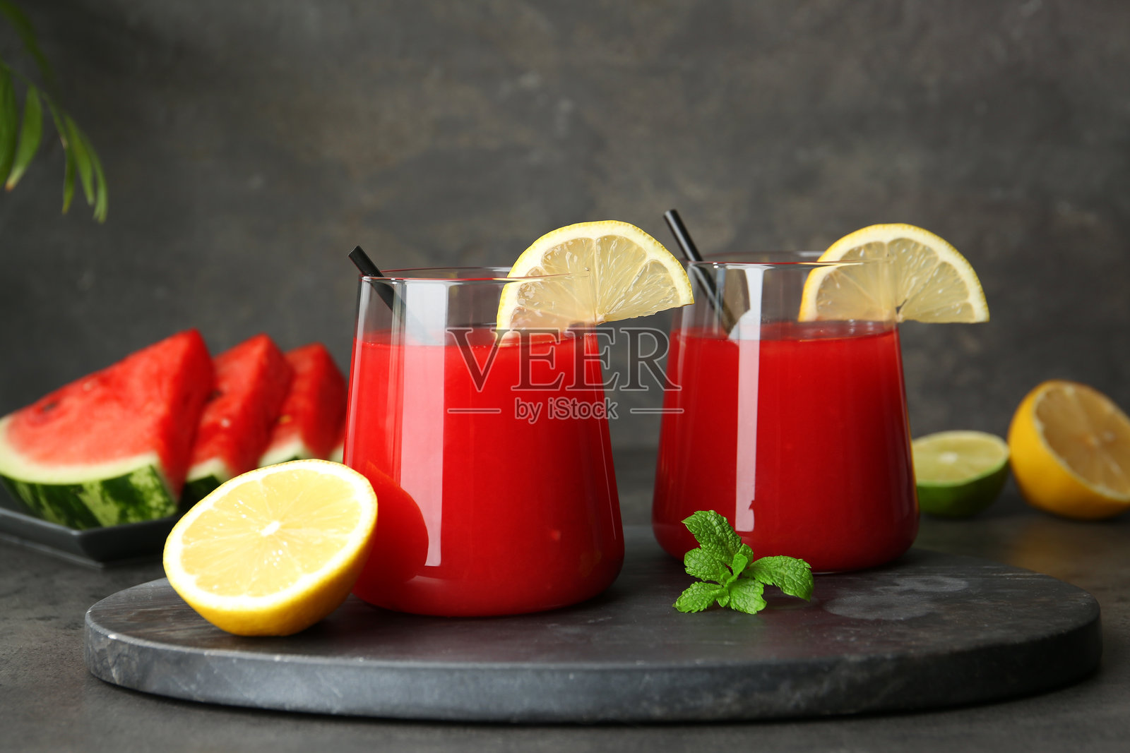 美味的西瓜饮料装在玻璃杯中,旁边有新鲜水果和薄荷,放在灰色桌子上。照片摄影图片