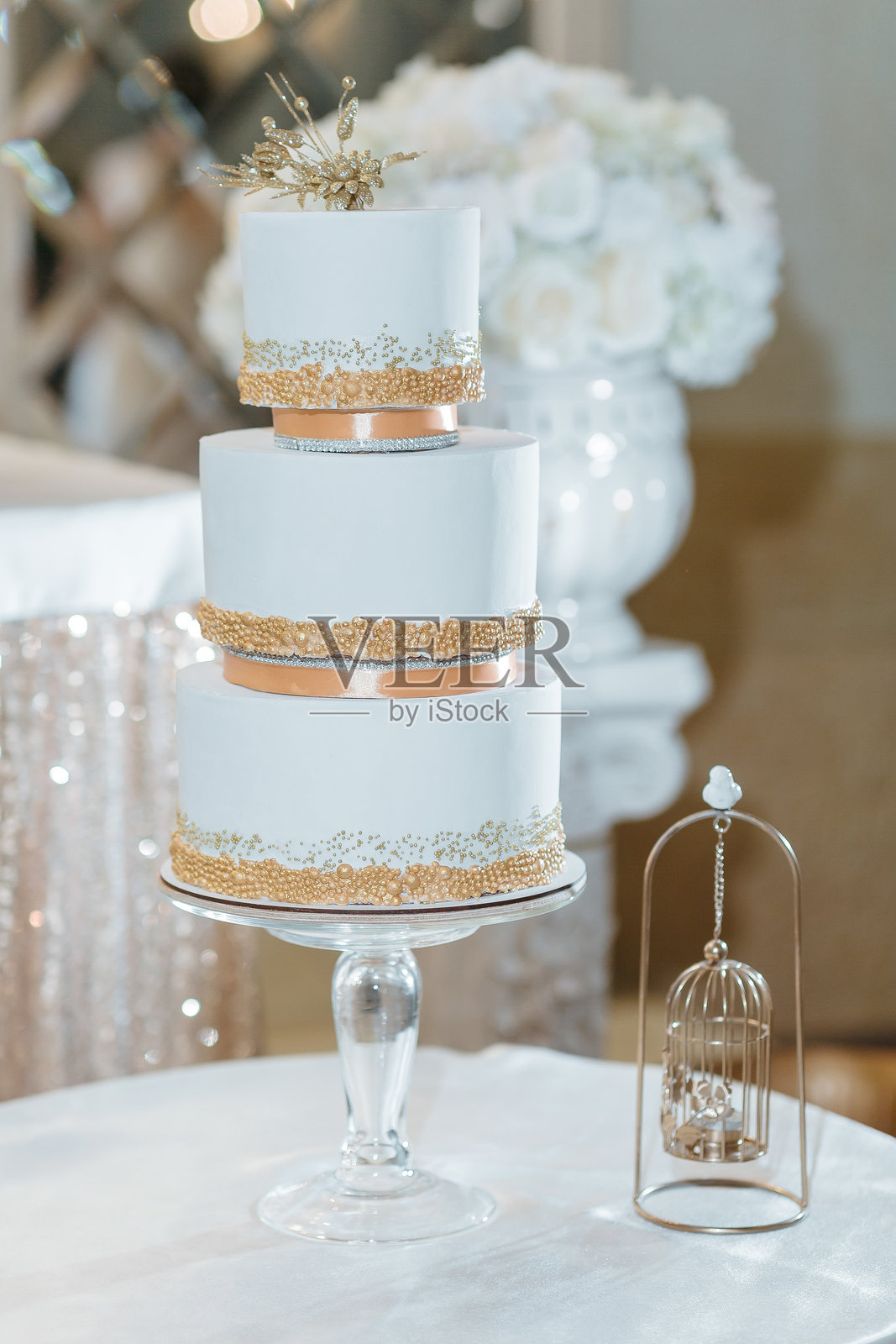 一个带有金色装饰的三层婚礼蛋糕放在玻璃支架上照片摄影图片