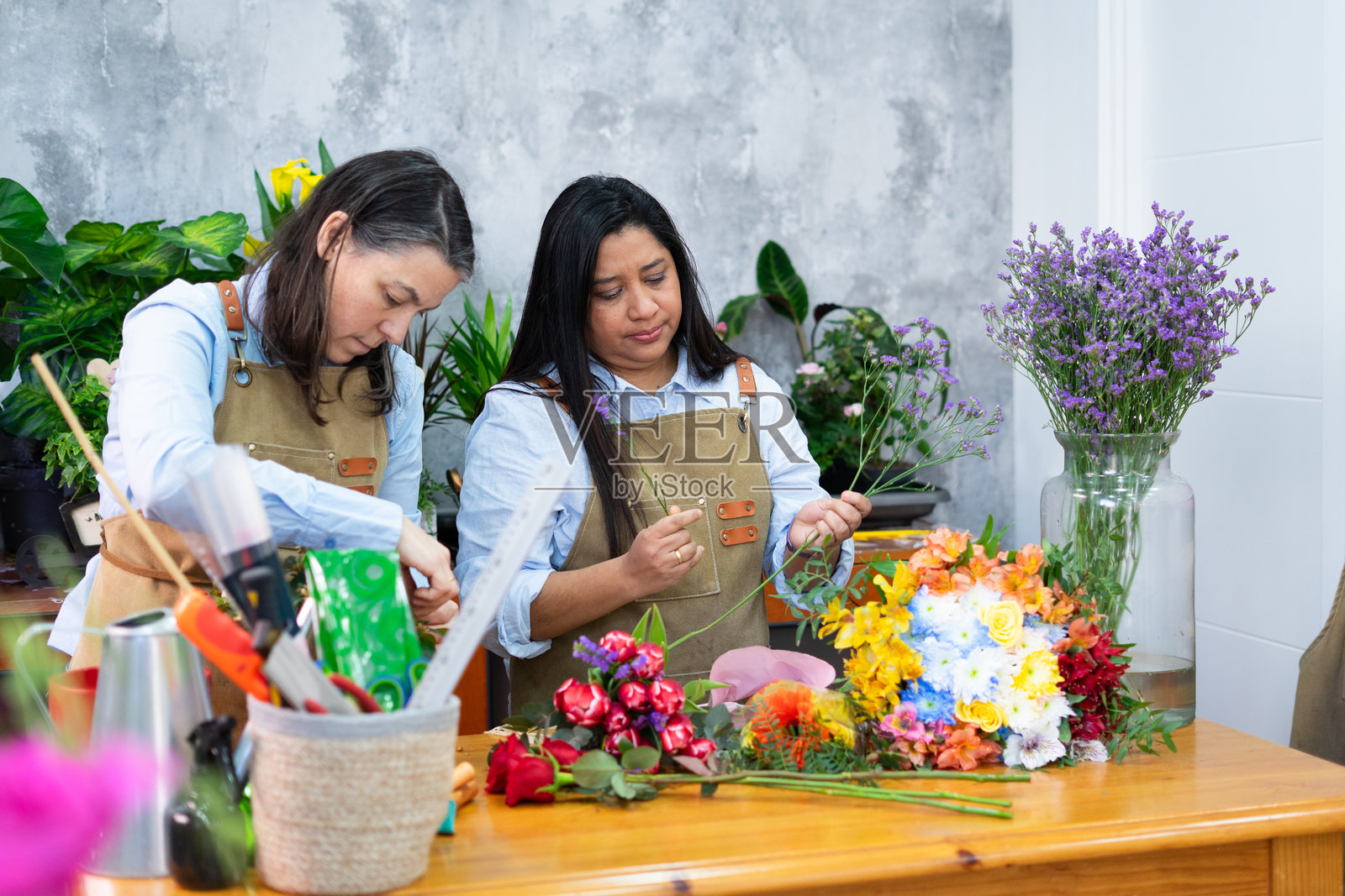 两位花店花艺师正在为一束色彩缤纷的花束进行插花安排照片摄影图片