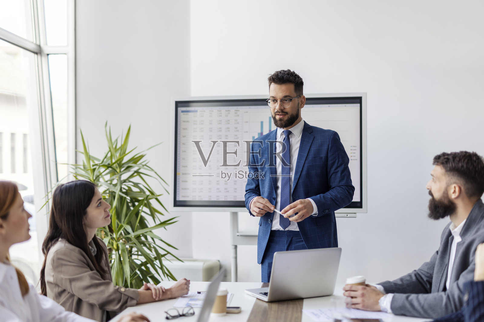 年轻团队领导站在会议桌前,向同事们发表演讲。照片摄影图片