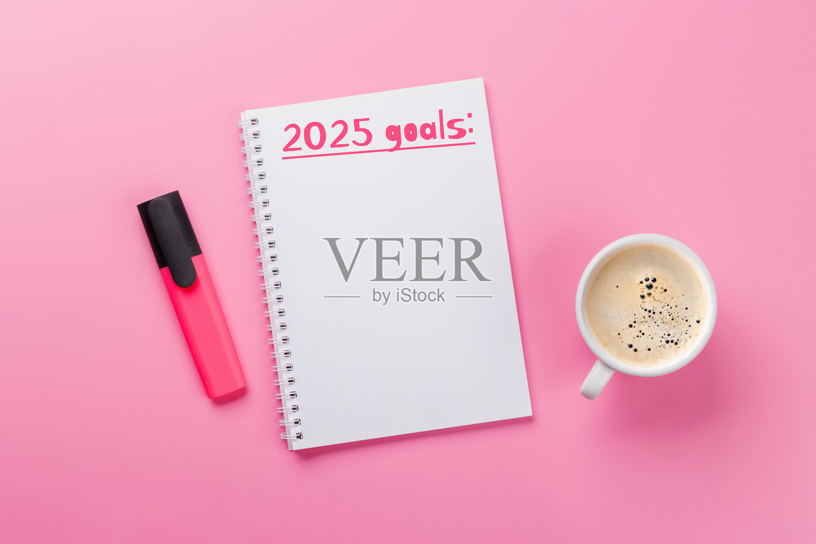现代粉色书桌,上面有咖啡、文具和一本标题为“2025目标”的记事本照片摄影图片