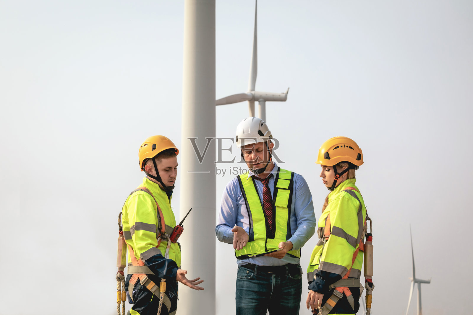 一组维护工程师正在使用平板电脑在风电场工作,并讨论清洁能源生产。未来替代可再生能源的概念。照片摄影图片