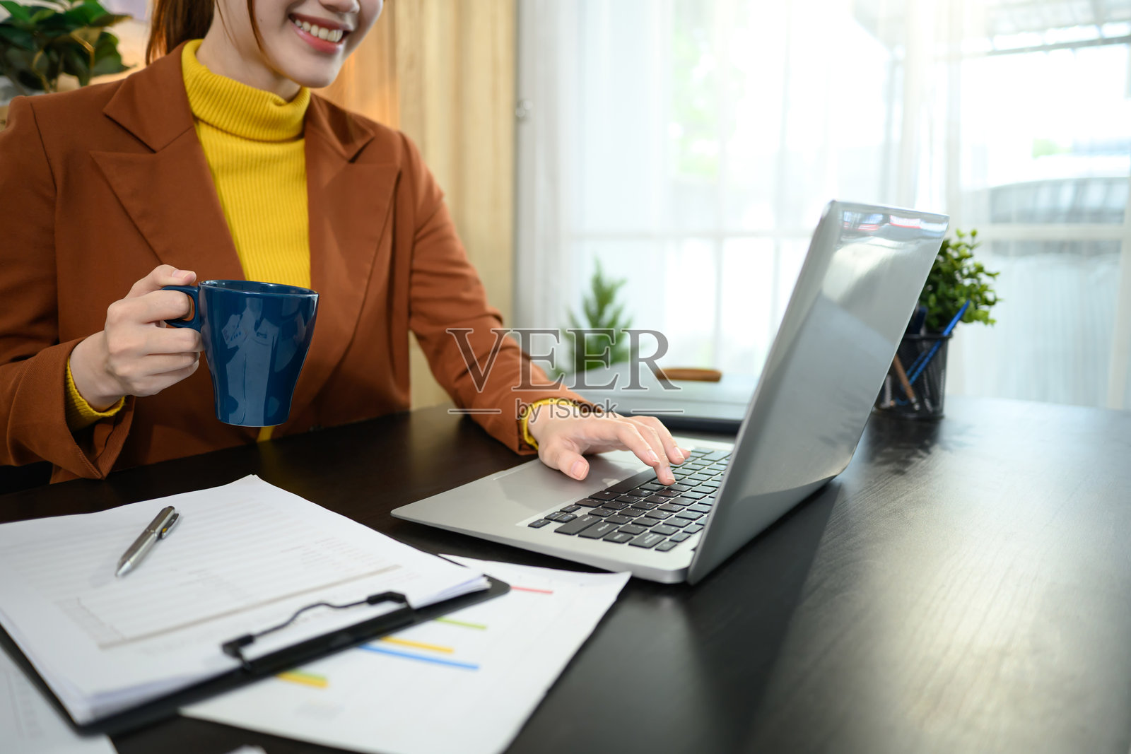 微笑的女商人手握咖啡杯,在桌子上使用笔记本电脑的特写镜头照片摄影图片