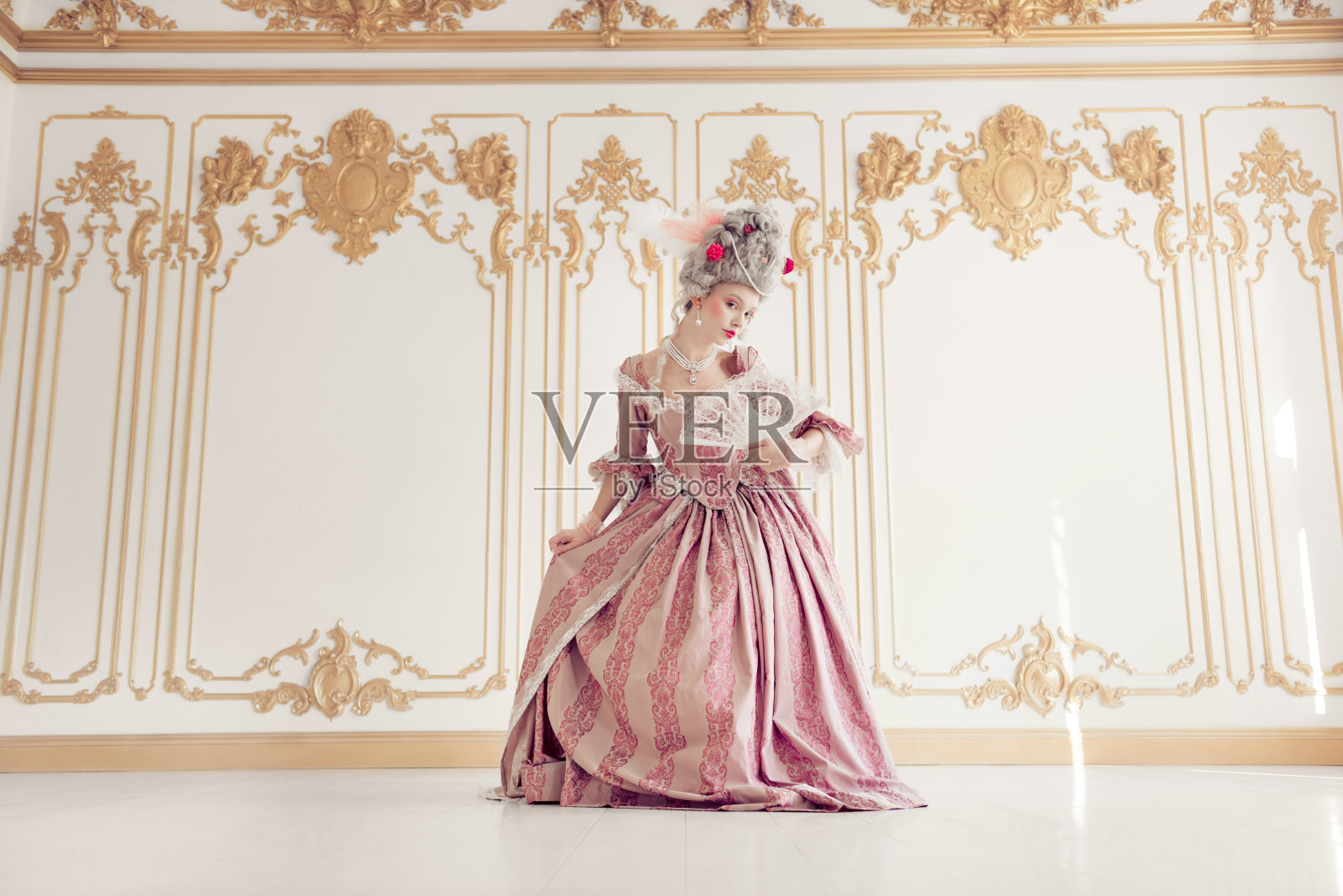 优雅的女性身穿粉色巴洛克长裙,在奢华的历史室内优雅地摆姿势,融合了过去与现在的时尚风格。照片摄影图片