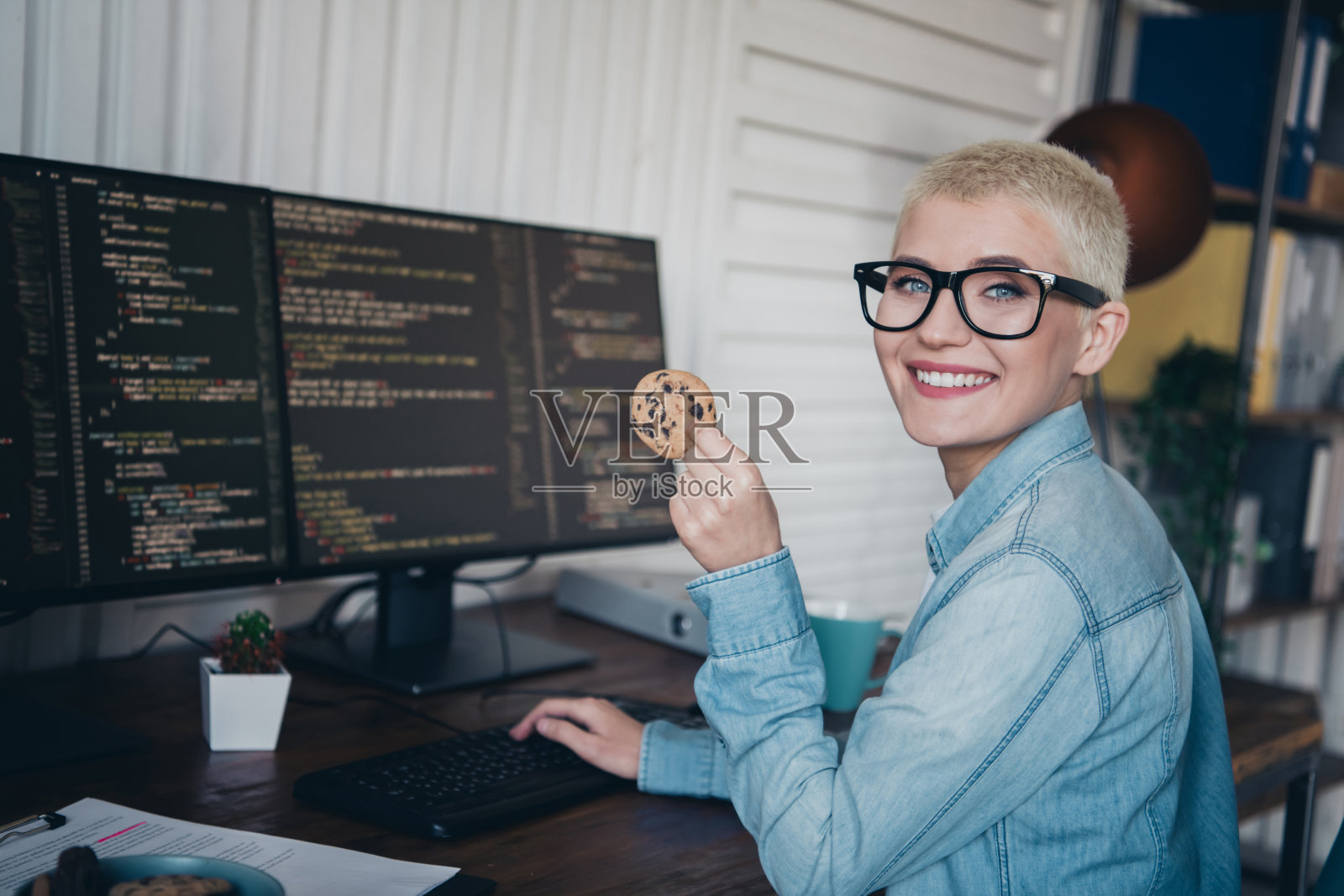 年轻女性在舒适的家庭办公室环境中享受饼干,同时进行编码项目。照片摄影图片