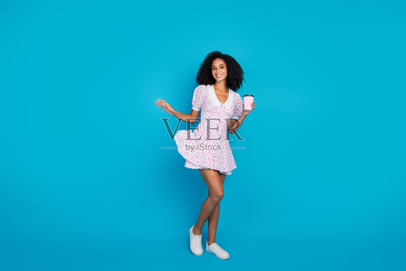 年轻时尚的女性穿着花卉印花裙,微笑着享受生活,背景是鲜艳的蓝色。照片摄影图片