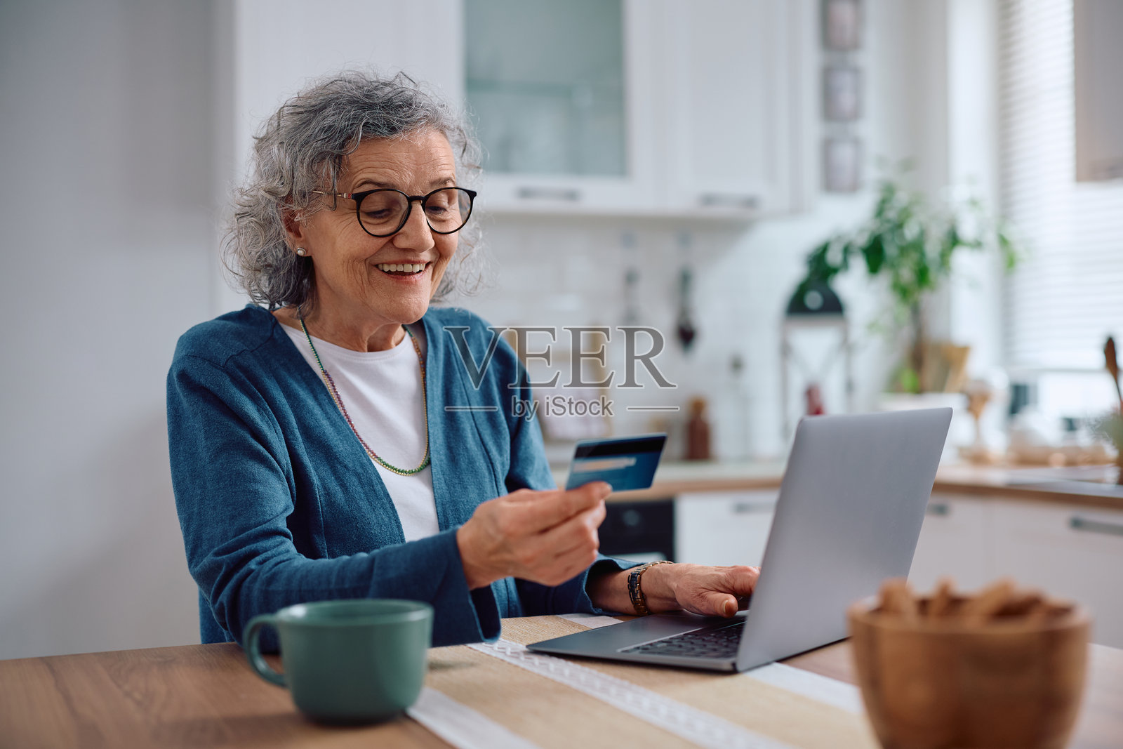 快乐的老年女性正在使用信用卡和笔记本电脑在线购物。照片摄影图片
