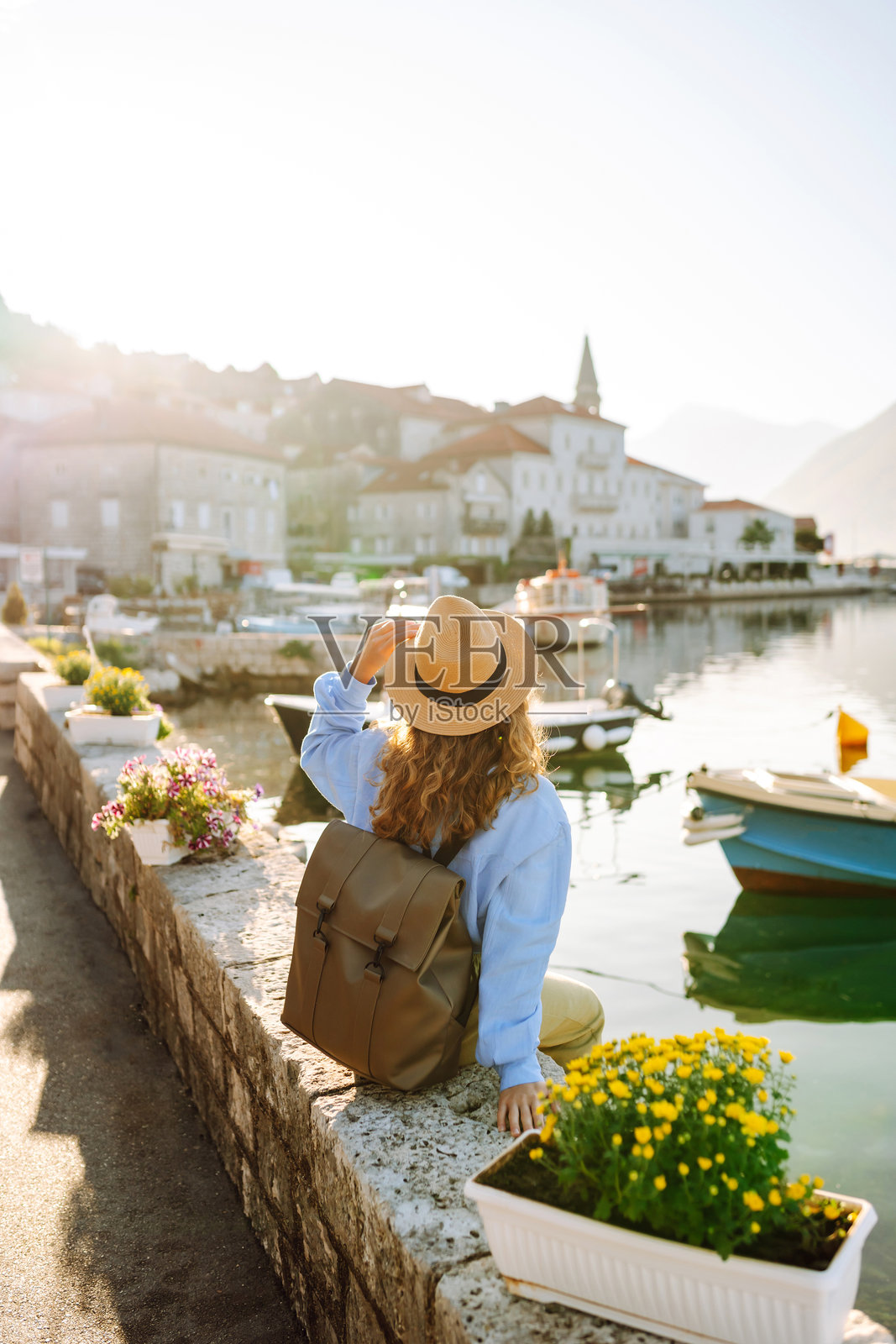 一位年轻游客背影,戴着帽子,背着背包,沿着滨水大道行走。照片摄影图片