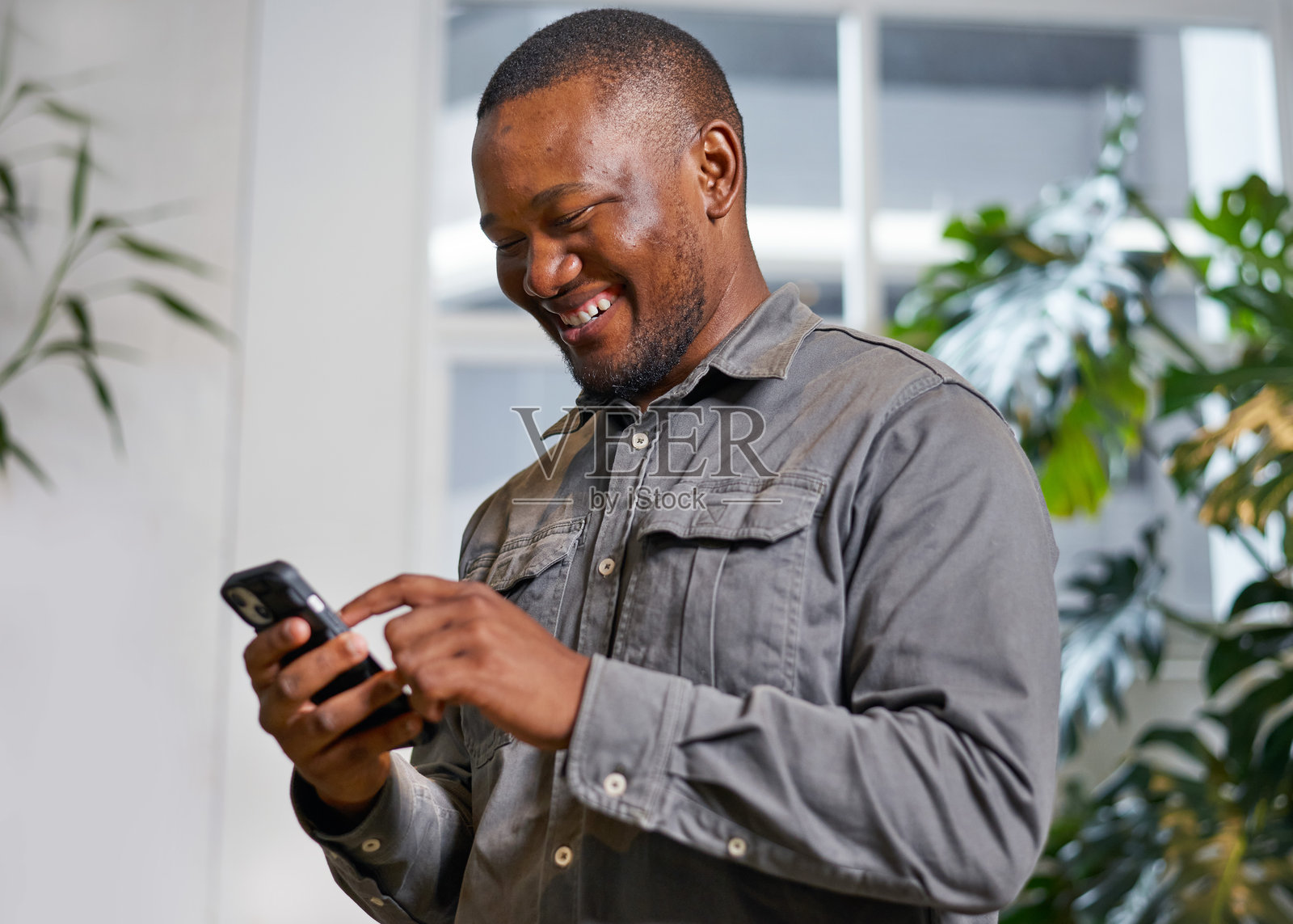 室内使用智能手机的男人微笑,背景是绿色植物照片摄影图片