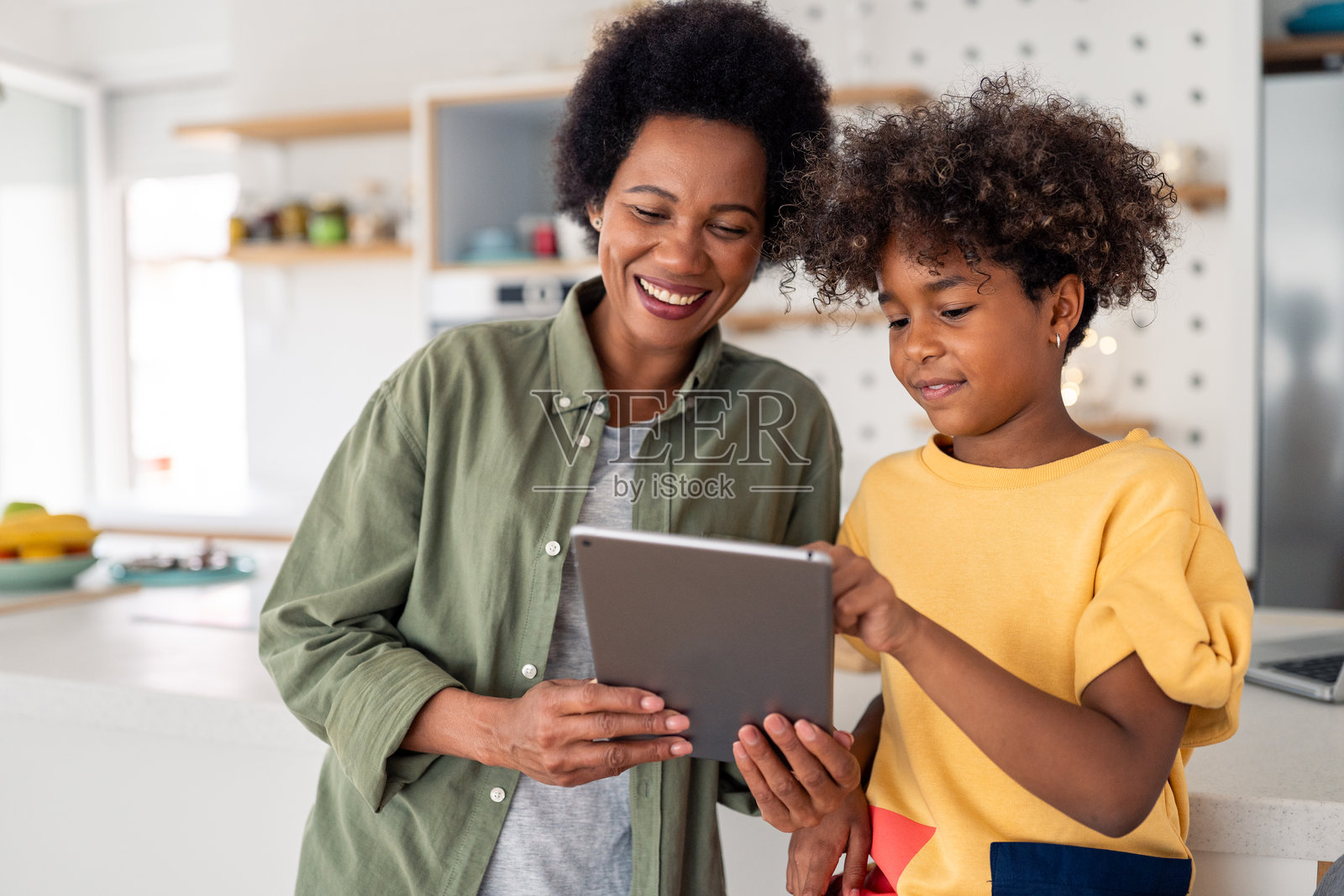 快乐的非洲母女在明亮的厨房里使用笔记本电脑,享受亲密时光。照片摄影图片