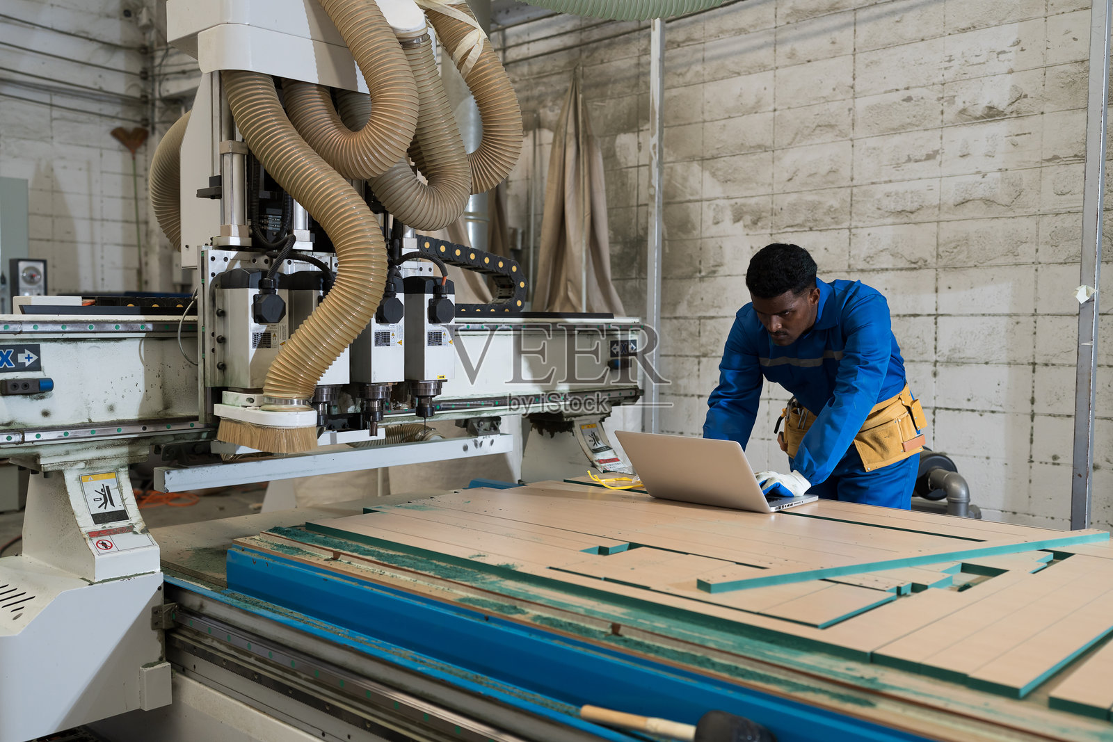 胶合板加工厂。家具制造。工程师在家具工厂使用笔记本电脑控制数控切割机。工业制造概念。照片摄影图片