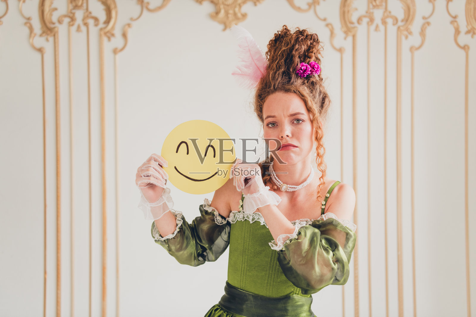 年轻女性穿着复古裙子,手持微笑面具,象征着现代情感与历史美学的融合,置身于优雅的室内环境中。照片摄影图片