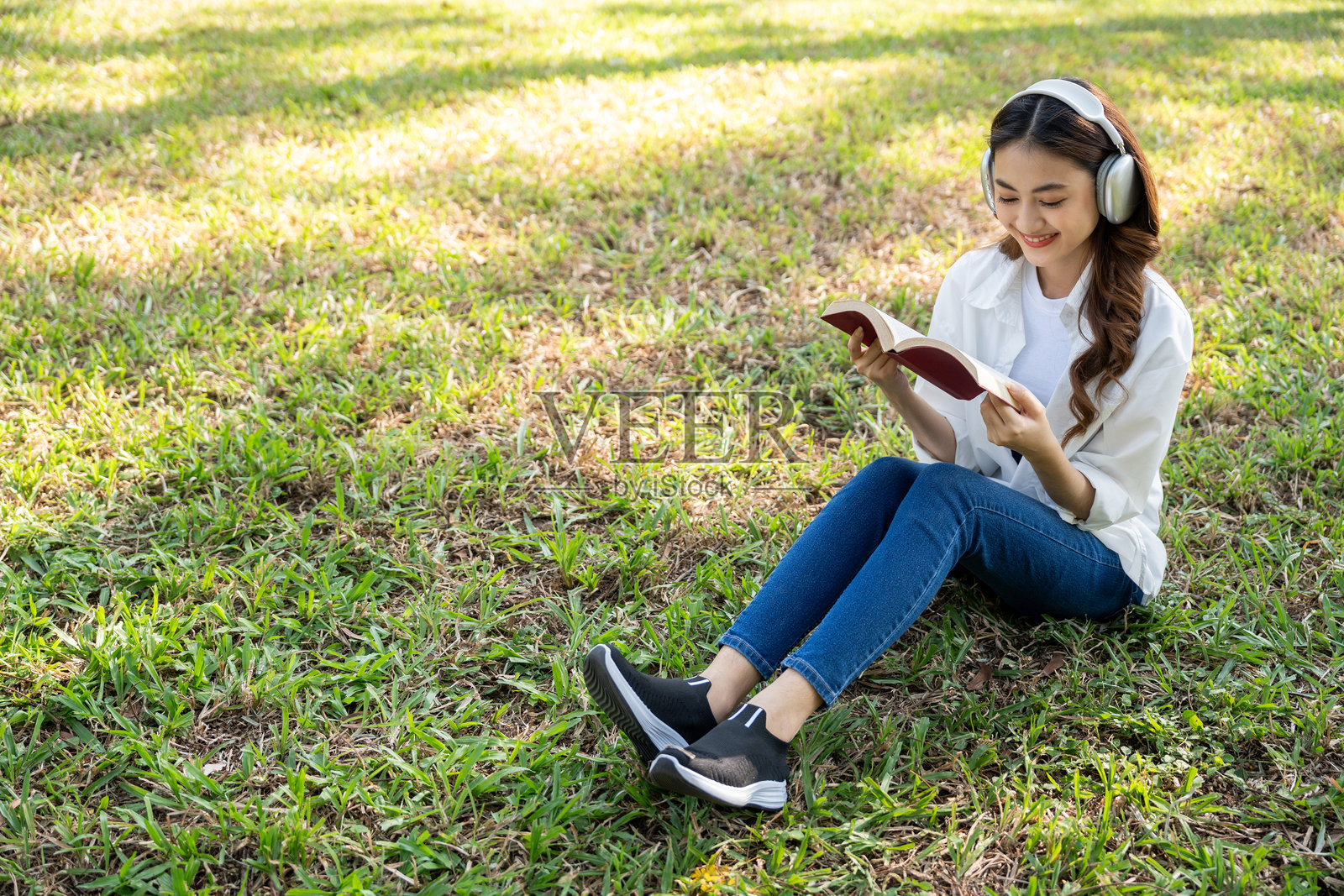 年轻的亚洲女性在公共公园放松,坐着阅读书籍。快乐的女性享受生活,享受大自然的时光。人与自然和谐共处。照片摄影图片