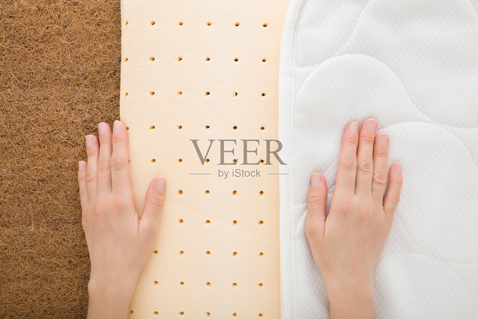 年轻女性的手触摸棕色椰壳纤维、黄色橡胶泡沫和白色布罩的矫形床垫,展示内部层次。特写镜头。俯视角度。照片摄影图片