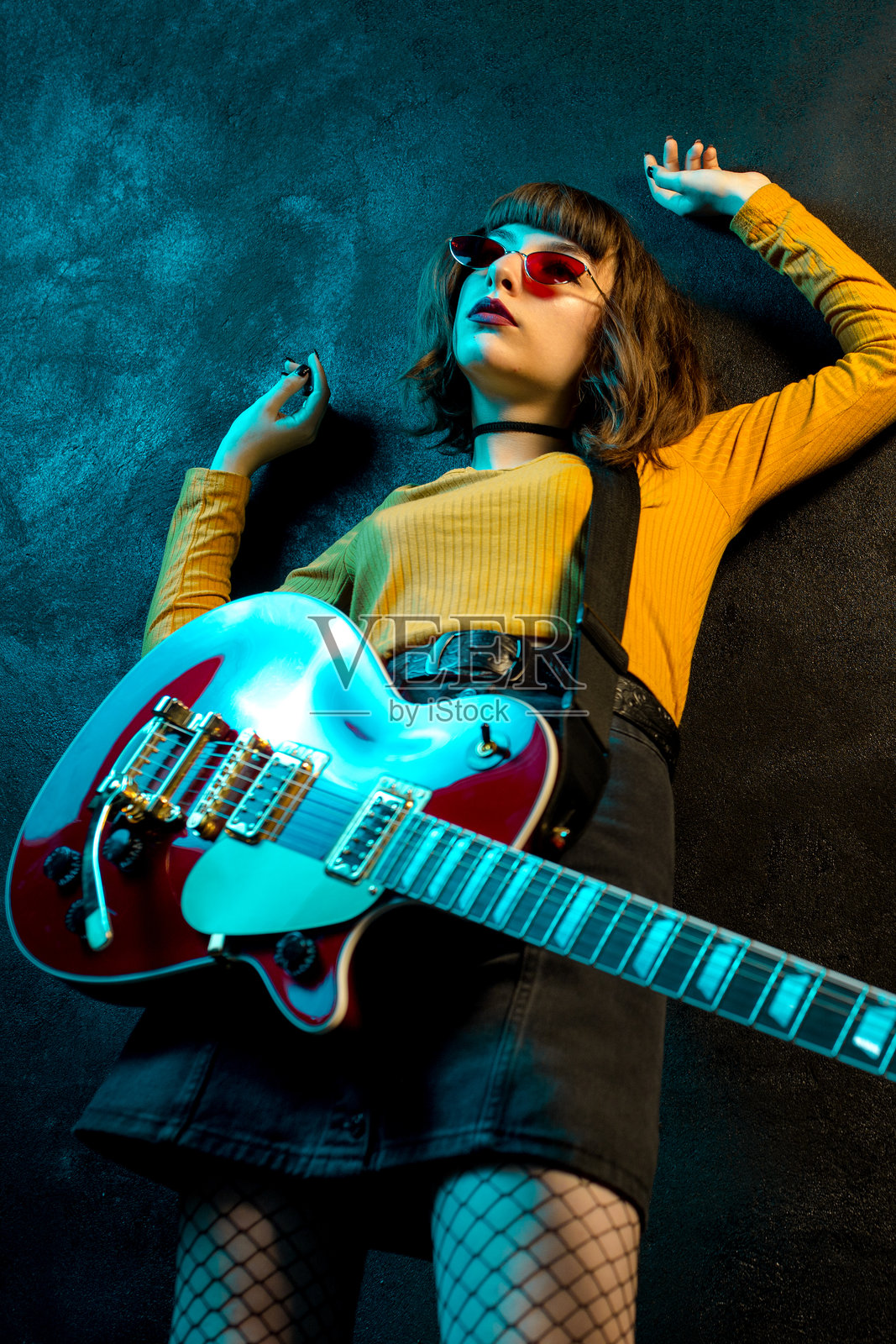 时尚的年轻嬉皮士女性,卷发,手持红色吉他,置身于霓虹灯下。摇滚音乐人摆姿势,手握电吉他。照片摄影图片