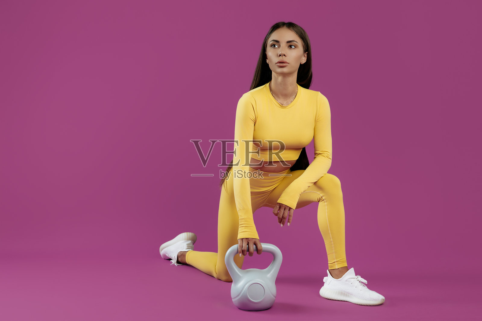 运动中的年轻棕发女性在紫色背景下休息,手中拿着灰色壶铃。照片摄影图片