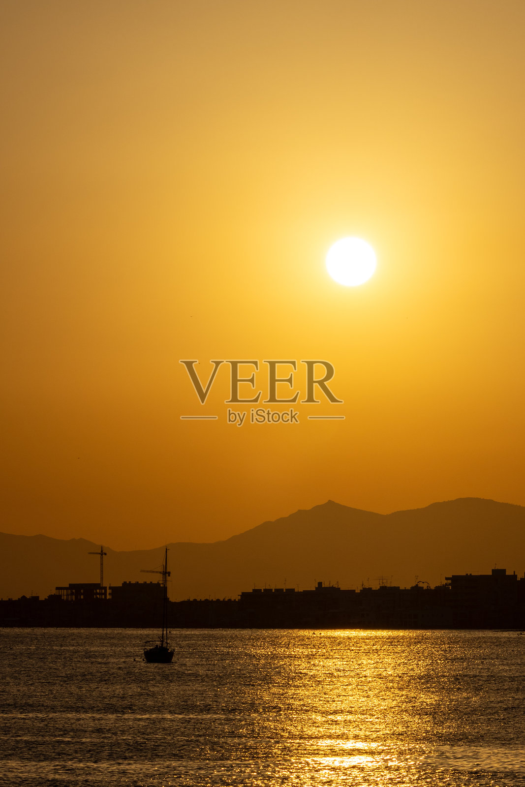 金色日落映照在平静的水面上,远处有剪影般的山脉和一只小船。照片摄影图片