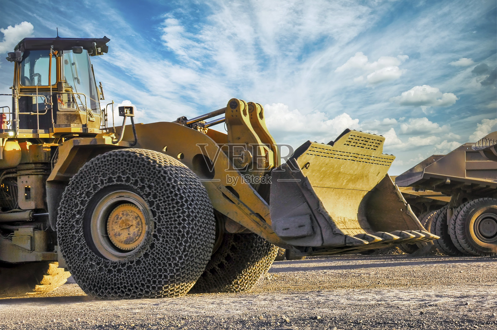 在钻石矿的轮式装载机旁停着矿用卡车,前轮装有链条以保护轮胎并增强抓地力,户外日落时分,蓝天和阳光透射。照片摄影图片